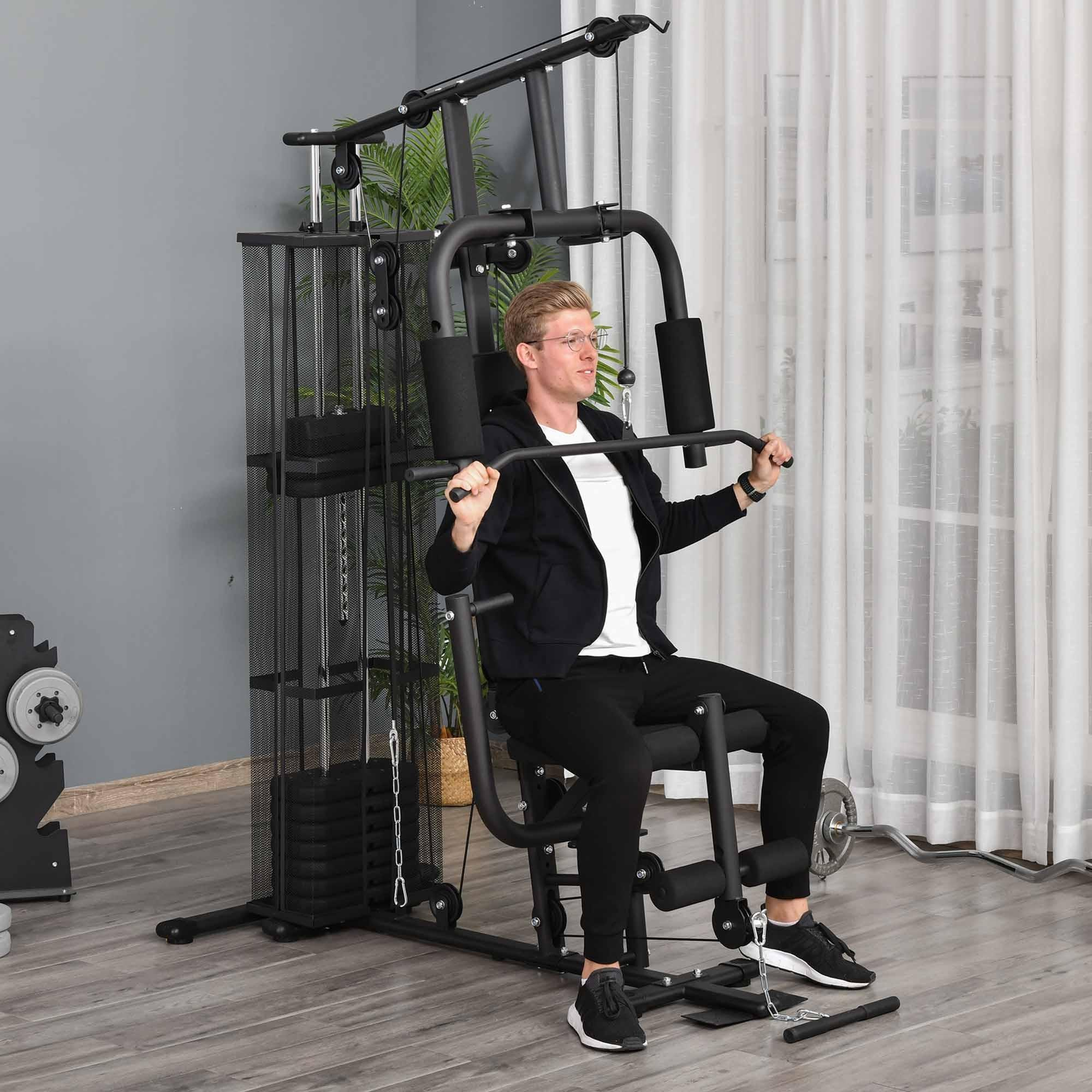 Mann benutzt Fitnessgerät. Er trägt Brille, schwarze Jacke und Hose. Gewichte im Hintergrund, in der Nähe eines Fensters.
