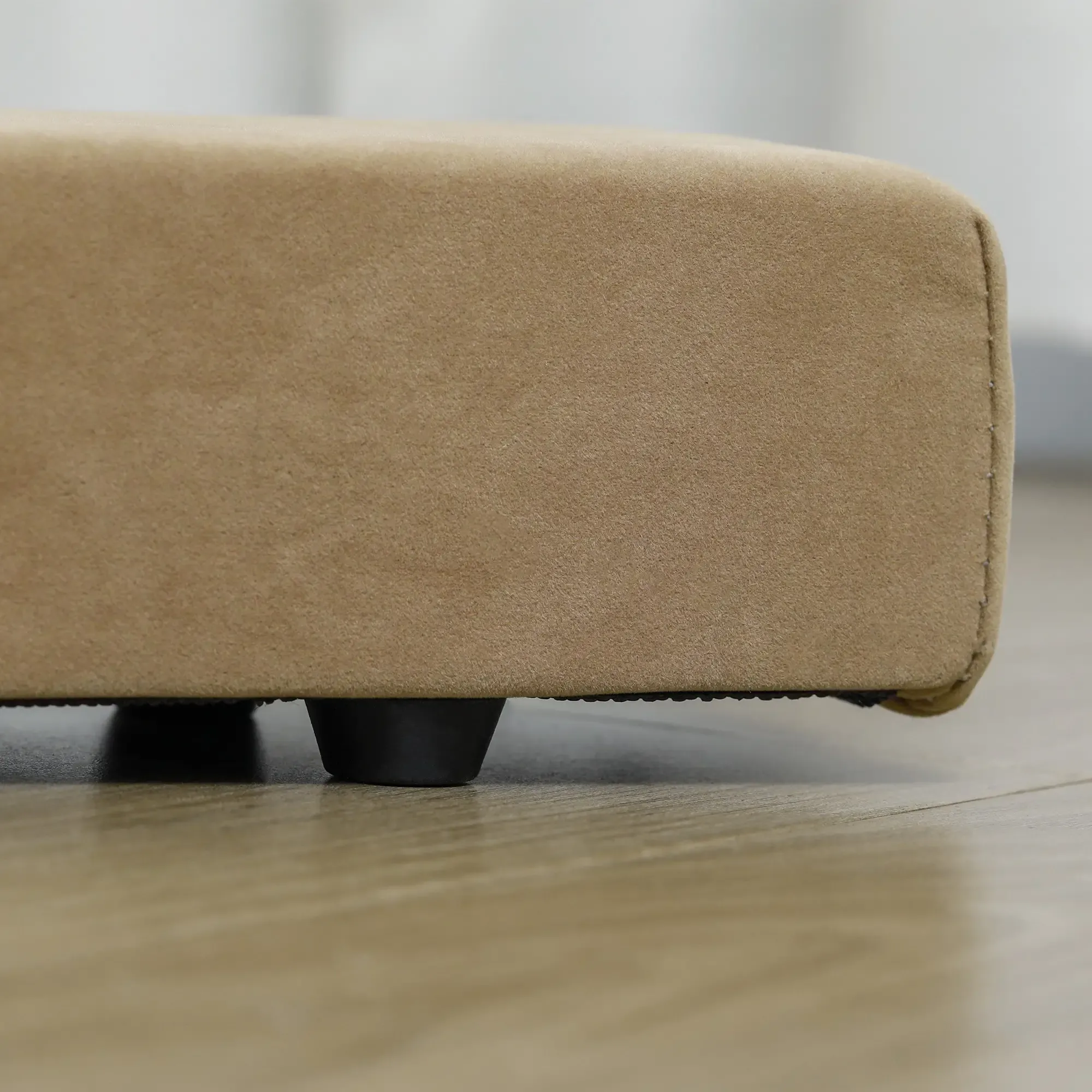 Beige Ottoman mit schwarzen Beinen auf hellem Holzboden. Weißer Vorhang im Hintergrund. Draufsicht.