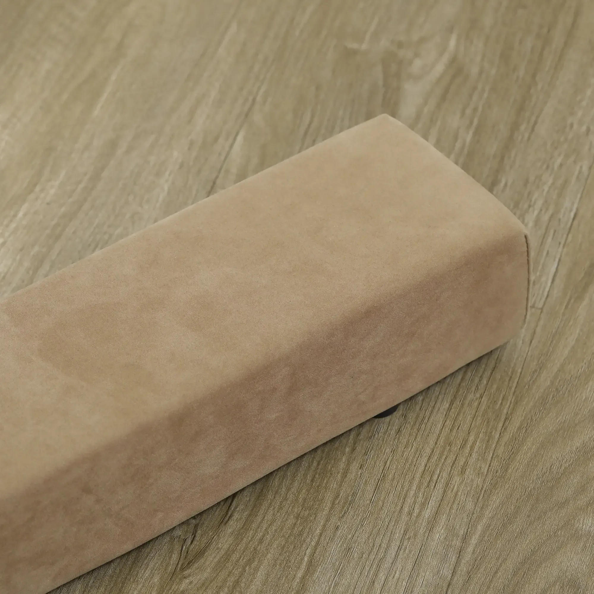 Ein beige rechteckiger Gegenstand auf einer Holzoberfläche. Der Gegenstand ist plüschig und hat abgerundete Ecken.