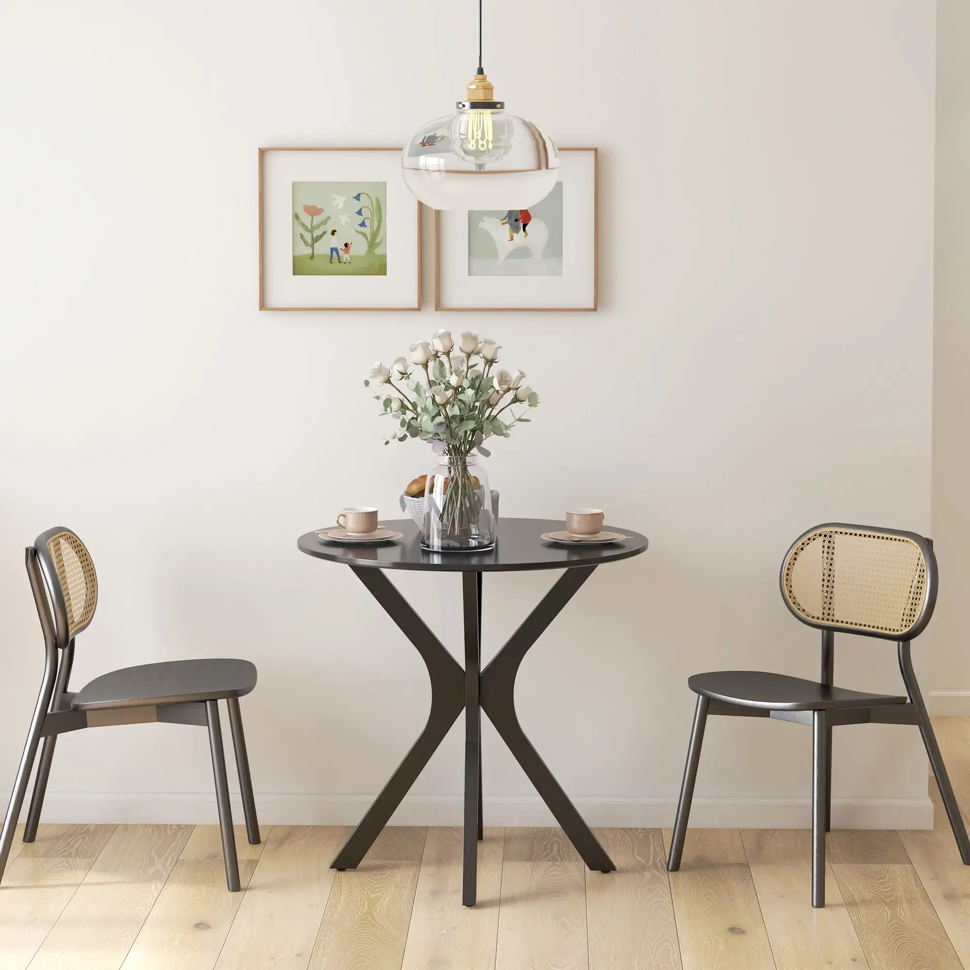Ein runder schwarzer Tisch mit zwei Stühlen, Blumen und zwei gerahmten Bildern stehen vor einer weißen Wand. Eine Lampe hängt oben.