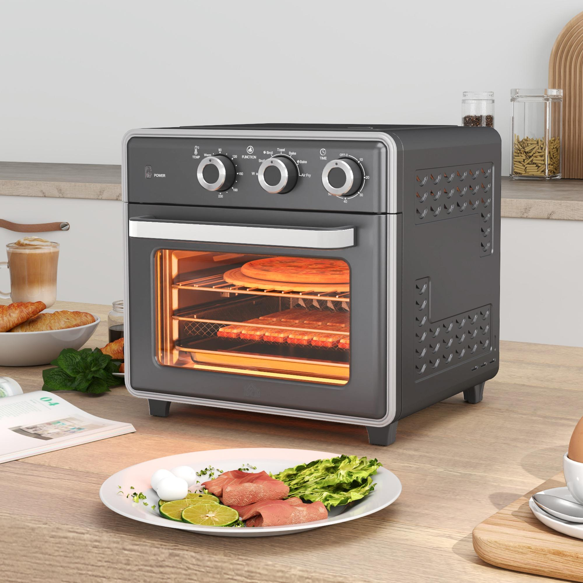 Ein Airfryer mit Pizza, daneben ein Teller mit Essen und andere Küchenutensilien auf einer Holzoberfläche.