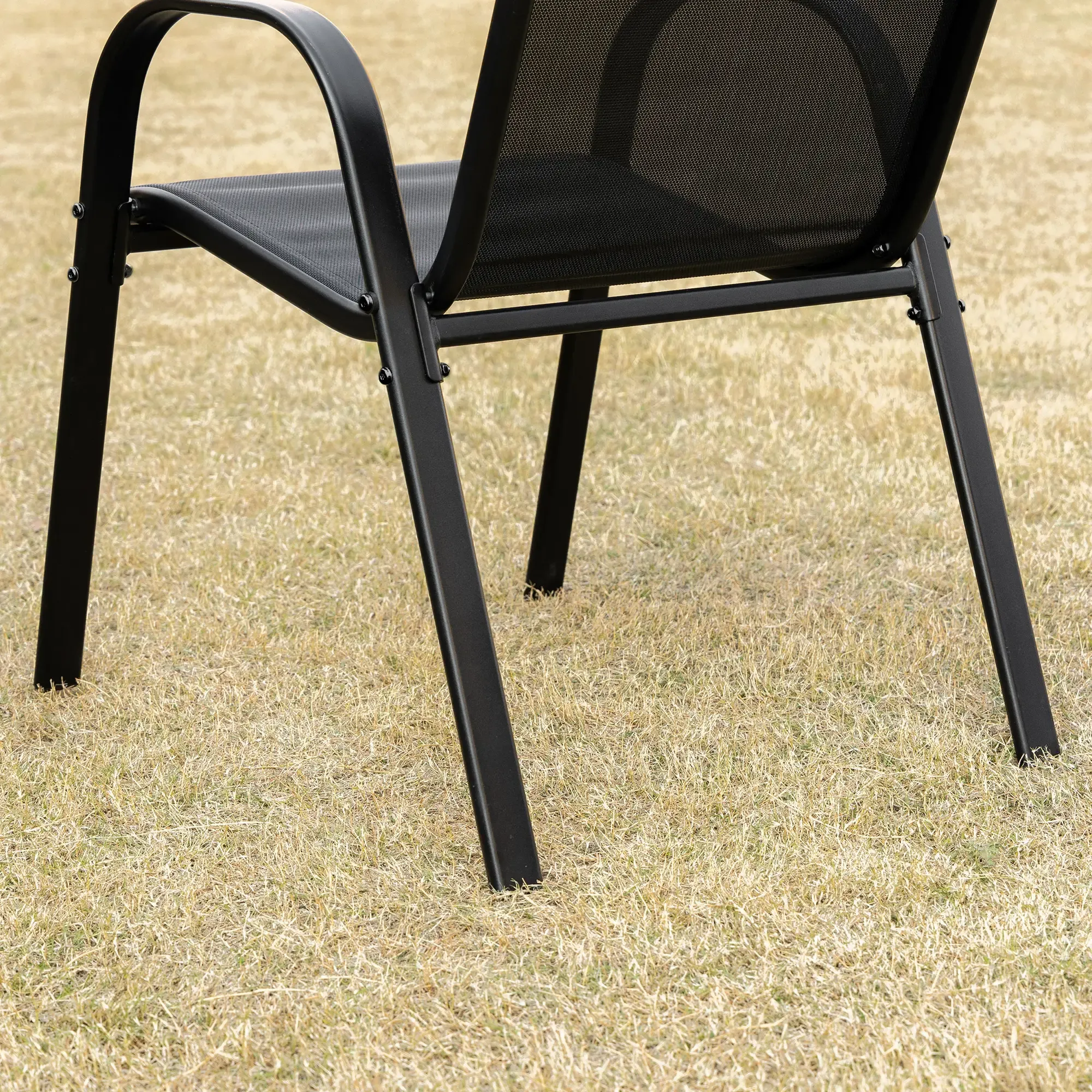 Nahaufnahme eines schwarzen Metallstuhls auf trockenem Gras. Rücken und Sitz sind sichtbar. Das Gras ist hellbraun.