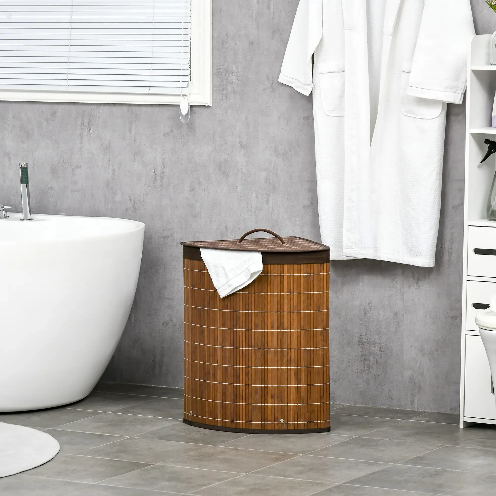 Badezimmer mit weißer Badewanne, Bambuskorb, weißem Bademantel und Fenster mit Jalousien. Graue Wand und Boden.