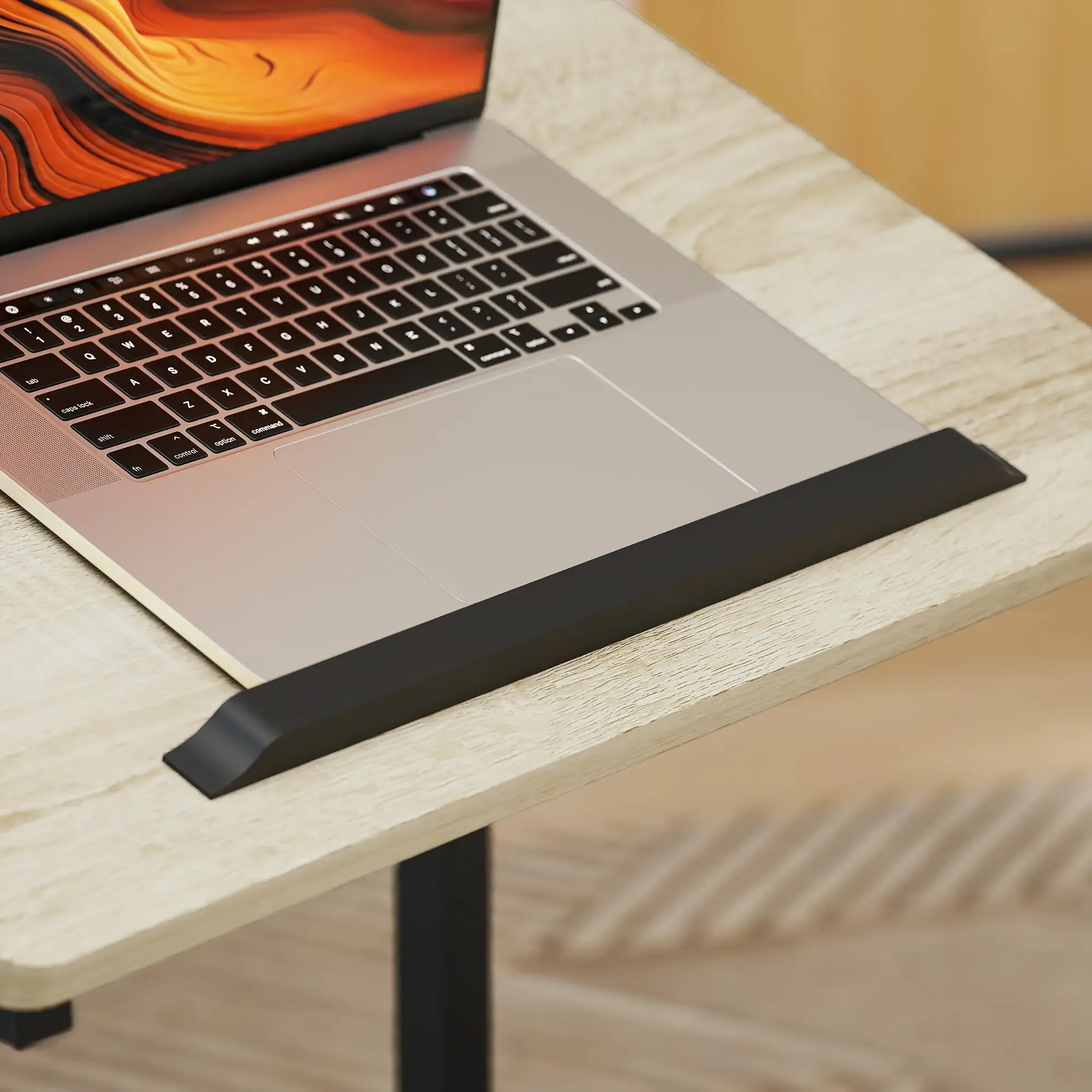 Ein Laptop auf einem Holztisch. Der Bildschirm zeigt ein oranges und gelbes abstraktes Design. Vorne befindet sich eine schwarze Handgelenkstütze.