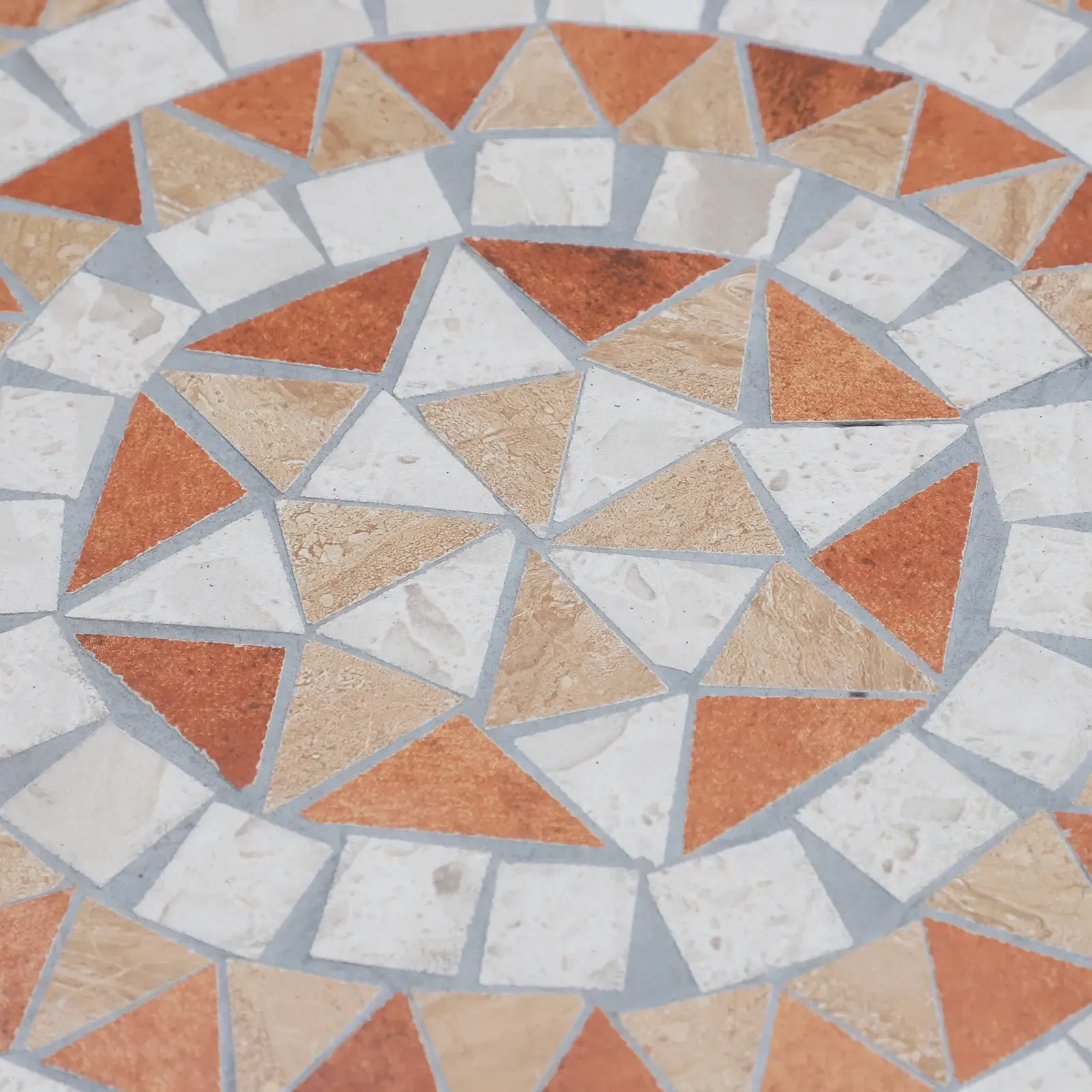 Nahaufnahme einer Mosaiktischplatte. Sie zeigt geometrische Muster aus Dreiecken und Quadraten in Orange-, Creme- und Beigetönen.