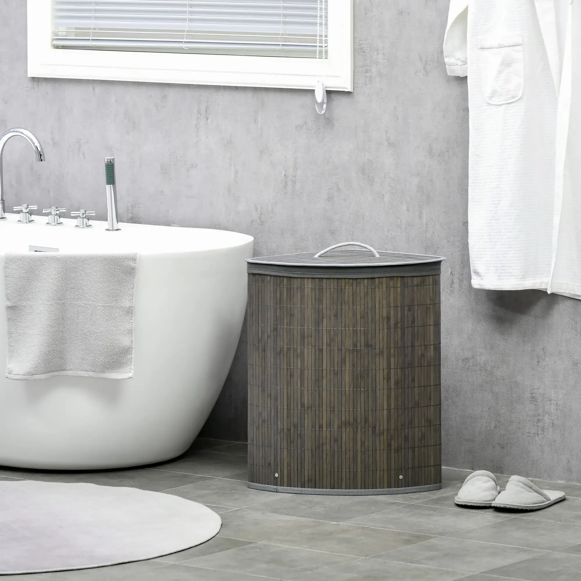 Badezimmer mit weißer Badewanne, grauem Wäschekorb und weißem Bademantel. Hausschuhe liegen auf dem Boden.