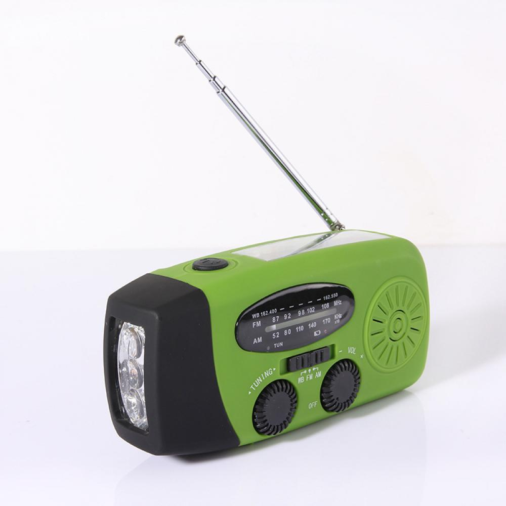 Ein grünes und schwarzes Radio mit Antenne. Es hat eine Taschenlampe und Knöpfe zum Einstellen. Das Radio steht auf weißem Untergrund.
