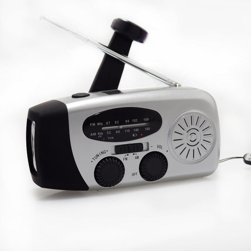 Ein silbernes und schwarzes Handkurbelradio. Es hat ein Einstellrad, eine Antenne und eine Lautstärkeregelung. Der Hintergrund ist weiß.
