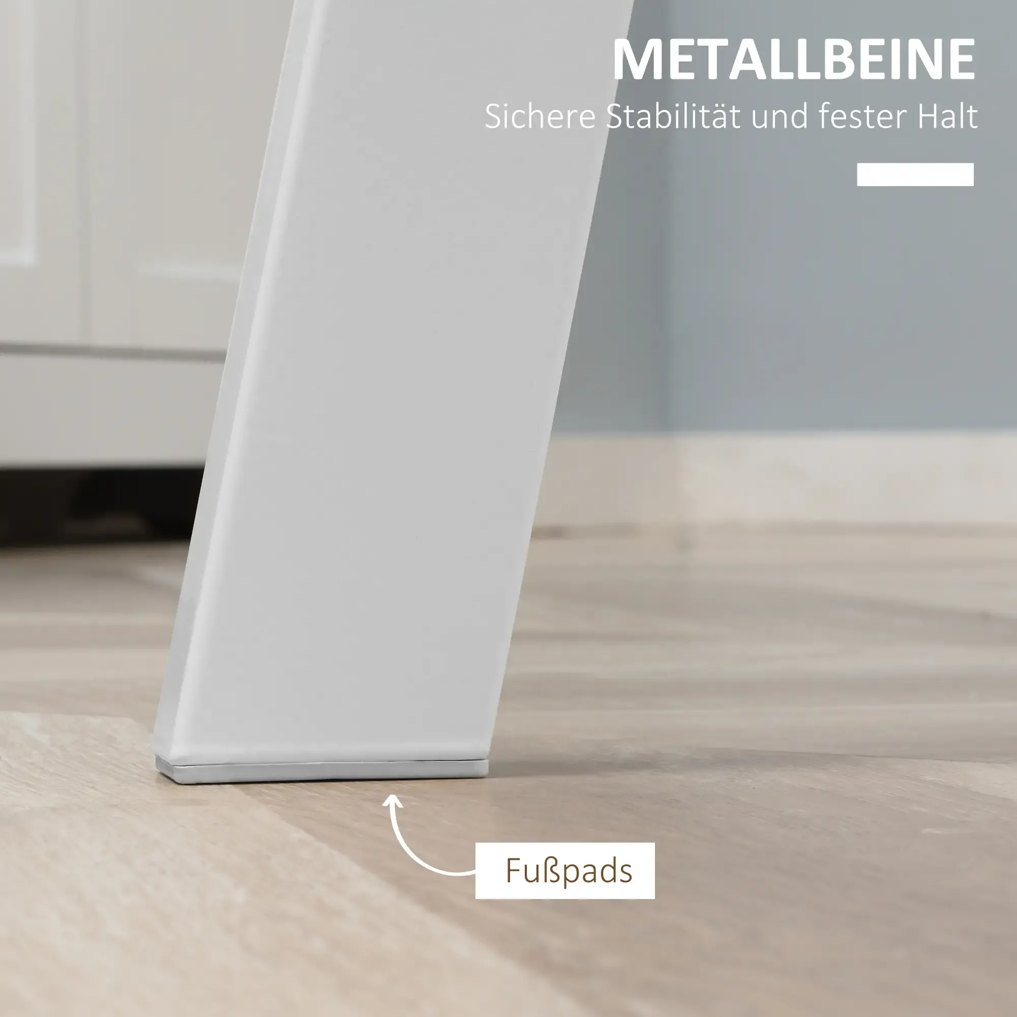 Nahaufnahme eines weißen Tischbeins mit Fußpad auf einem Holzboden. Der Hintergrund zeigt eine Wand und einen Schrank.