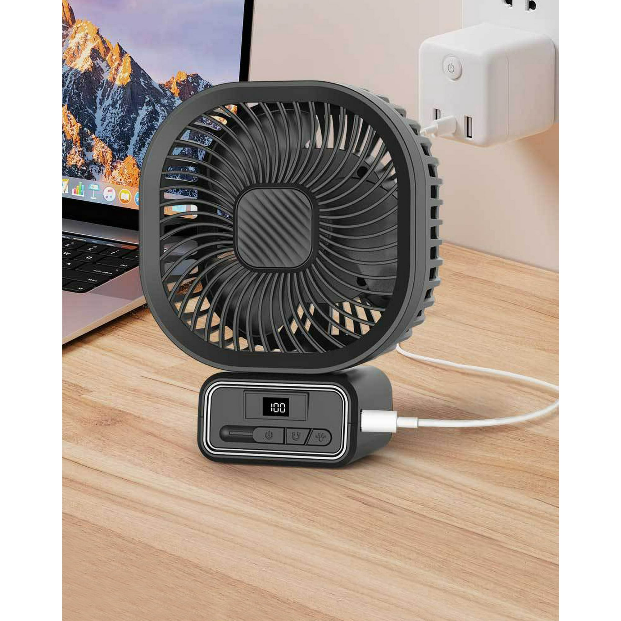 Ein schwarzer Ventilator steht auf einem Holztisch und ist an einen Wandadapter angeschlossen. Im Hintergrund befindet sich ein Laptop.