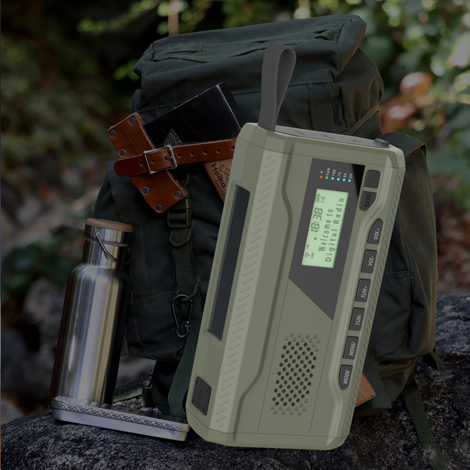 Ein olivgrünes Digitalradio, ein Rucksack, eine Wasserflasche und eine Axt im Hintergrund. Das Radio zeigt die Uhrzeit und 'Welcome to Digital Radio'.