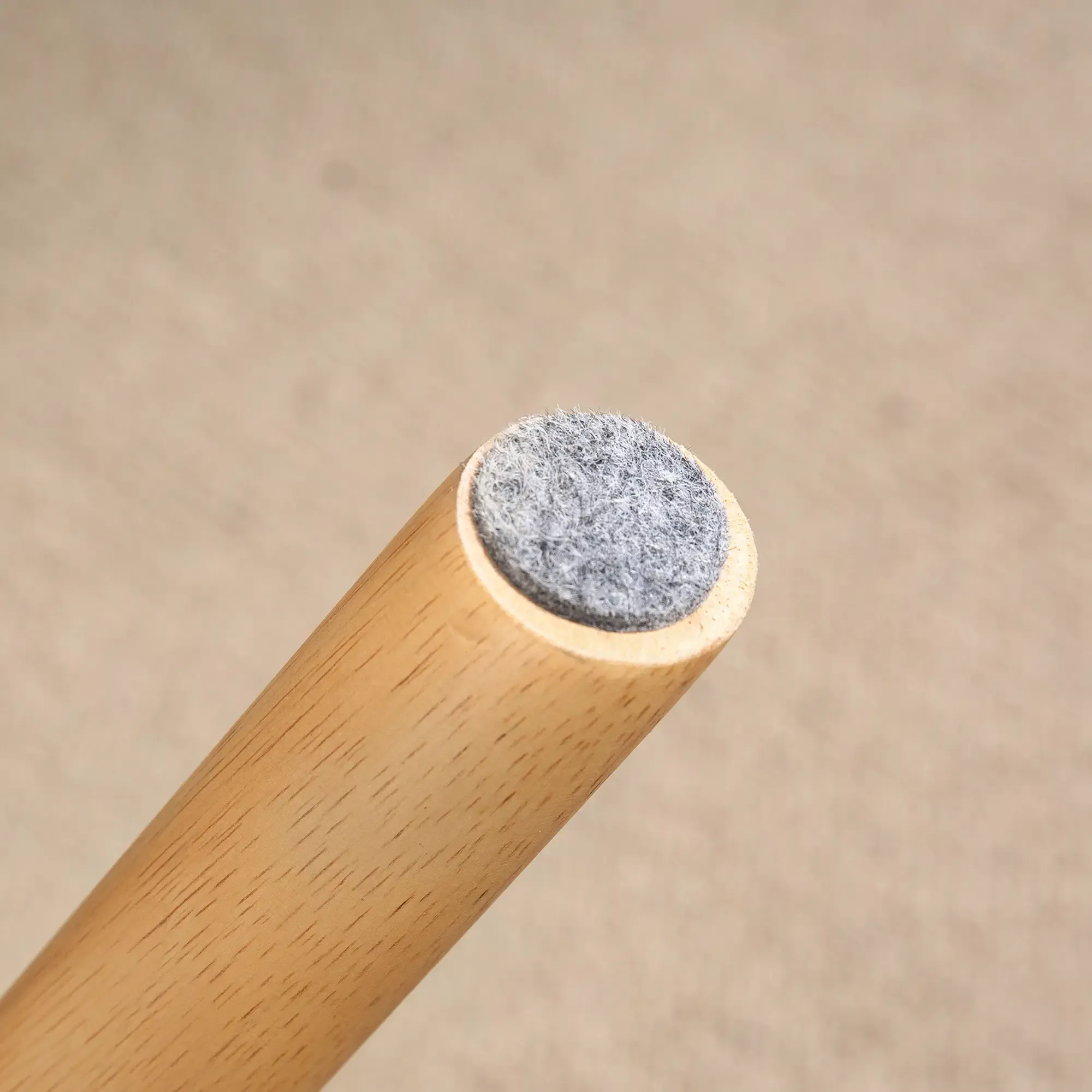 Holzbein mit grauem Filzpad am Boden. Der Hintergrund ist eine hellbraune Oberfläche.