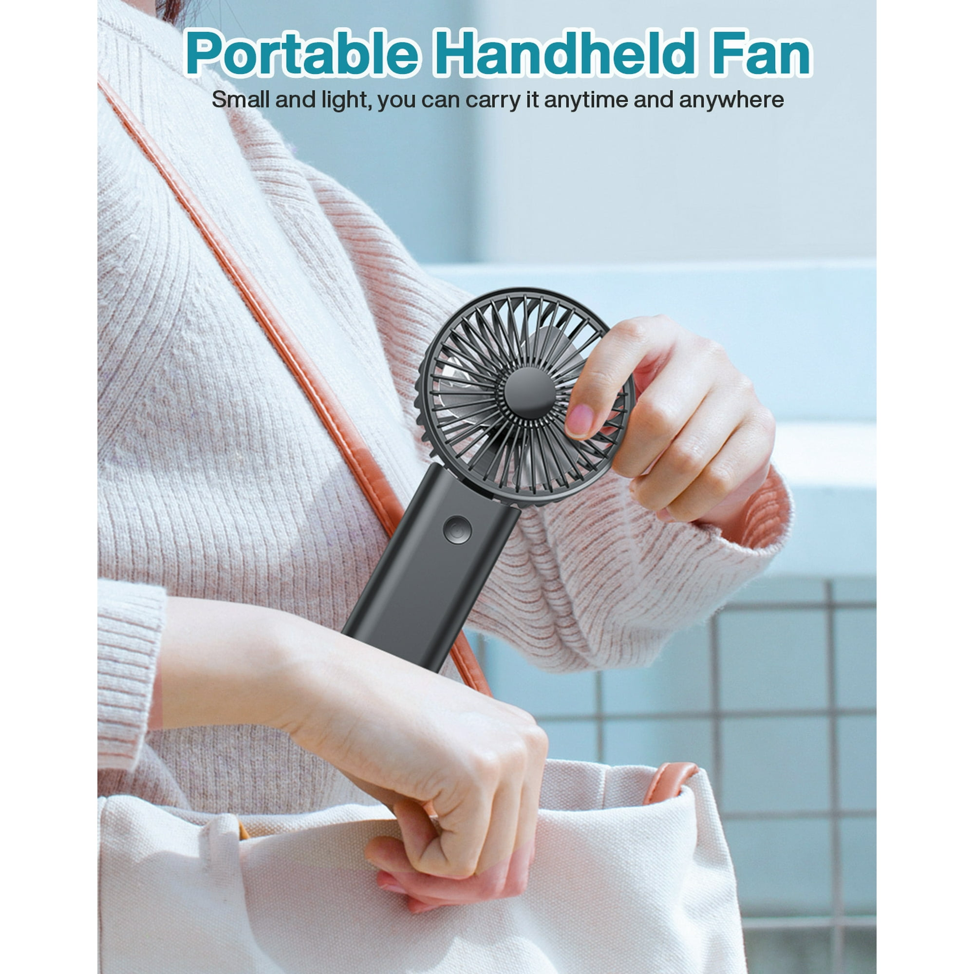 Eine Person hält einen schwarzen tragbaren Ventilator. Sie trägt einen Pullover und hält eine beigefarbene Tragetasche.