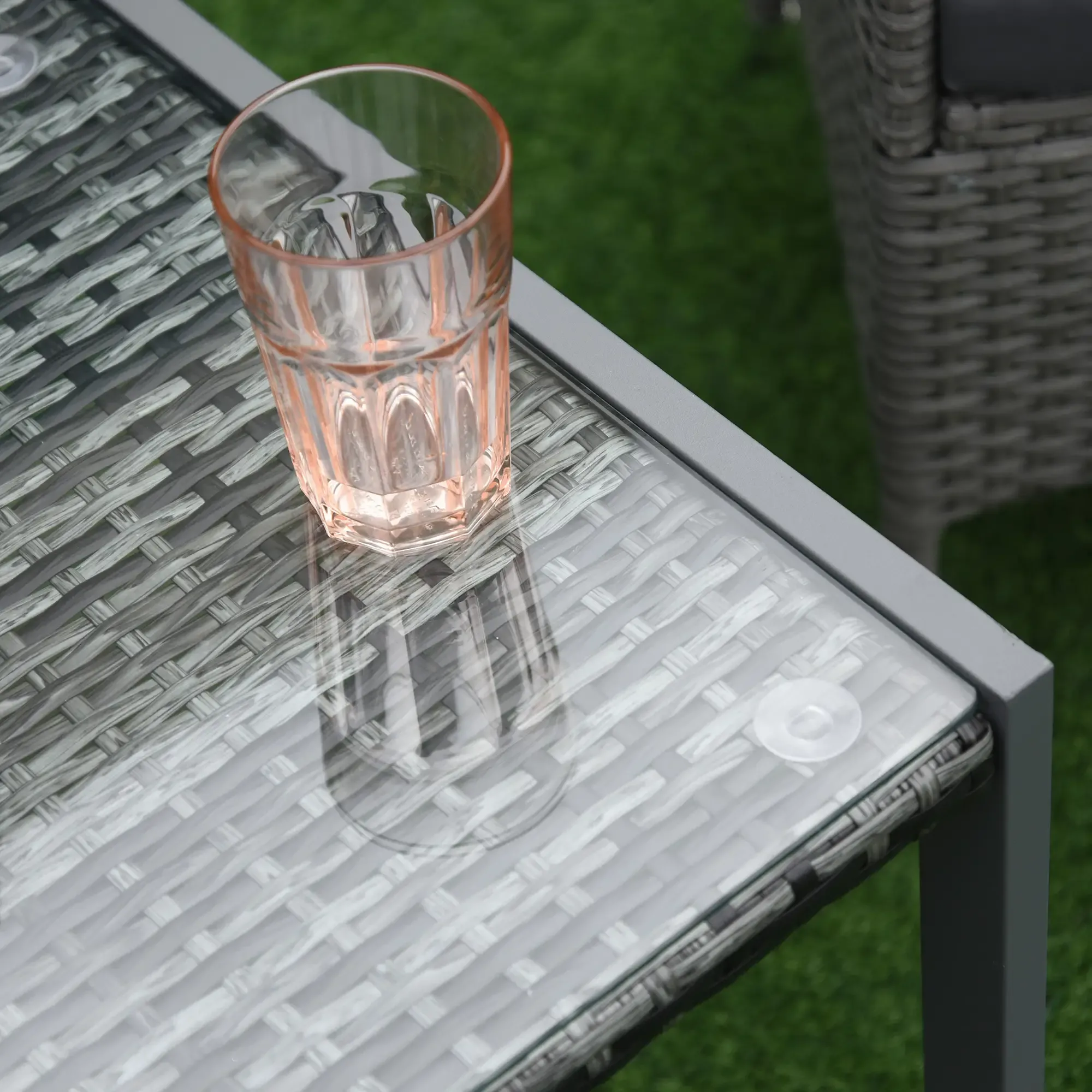 Ein Glas rosa Flüssigkeit steht auf einem Glastisch. Der Tisch steht auf einer grünen Oberfläche. Ein Korbstuhl ist sichtbar.