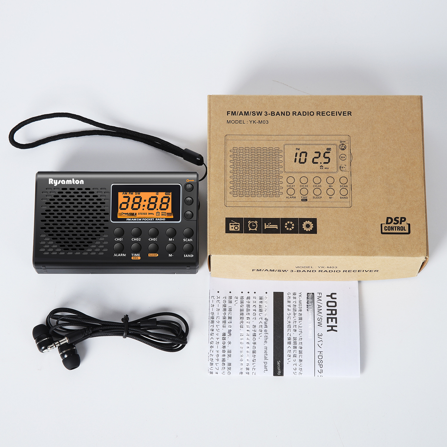 Ein schwarzes Radio mit Digitalanzeige, Kopfhörern und einer Schachtel liegen auf weißem Untergrund.