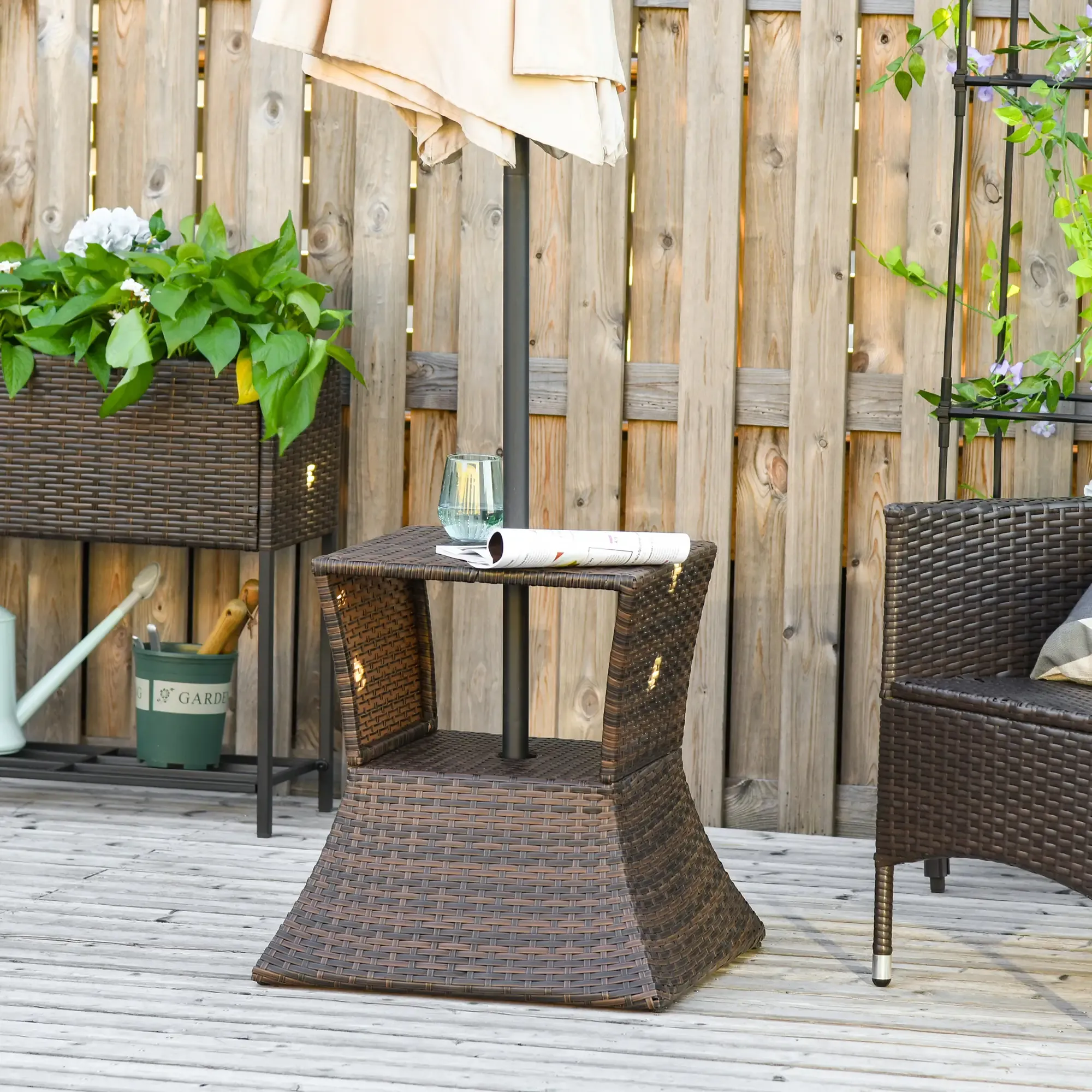 Szene auf der Terrasse: Brauner gewebter Tisch mit Glas und Zeitung, Sonnenschirm, Stuhl, Pflanzen und Holzzaun im Hintergrund.