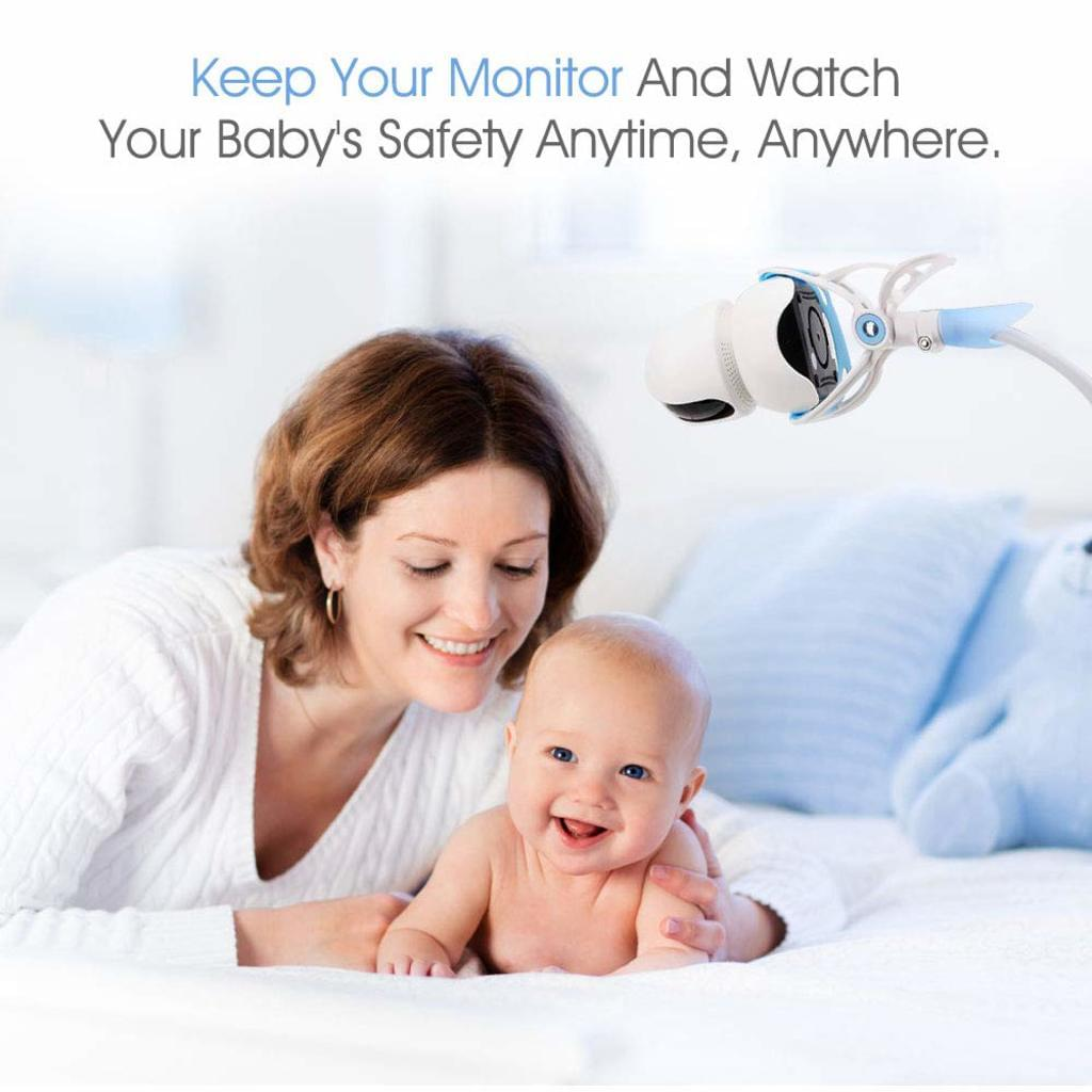 Eine lächelnde Mutter hält ein Baby auf einem Bett. Über ihnen befindet sich ein Babyphone. Der Hintergrund hat Kissen und ein Stofftier.