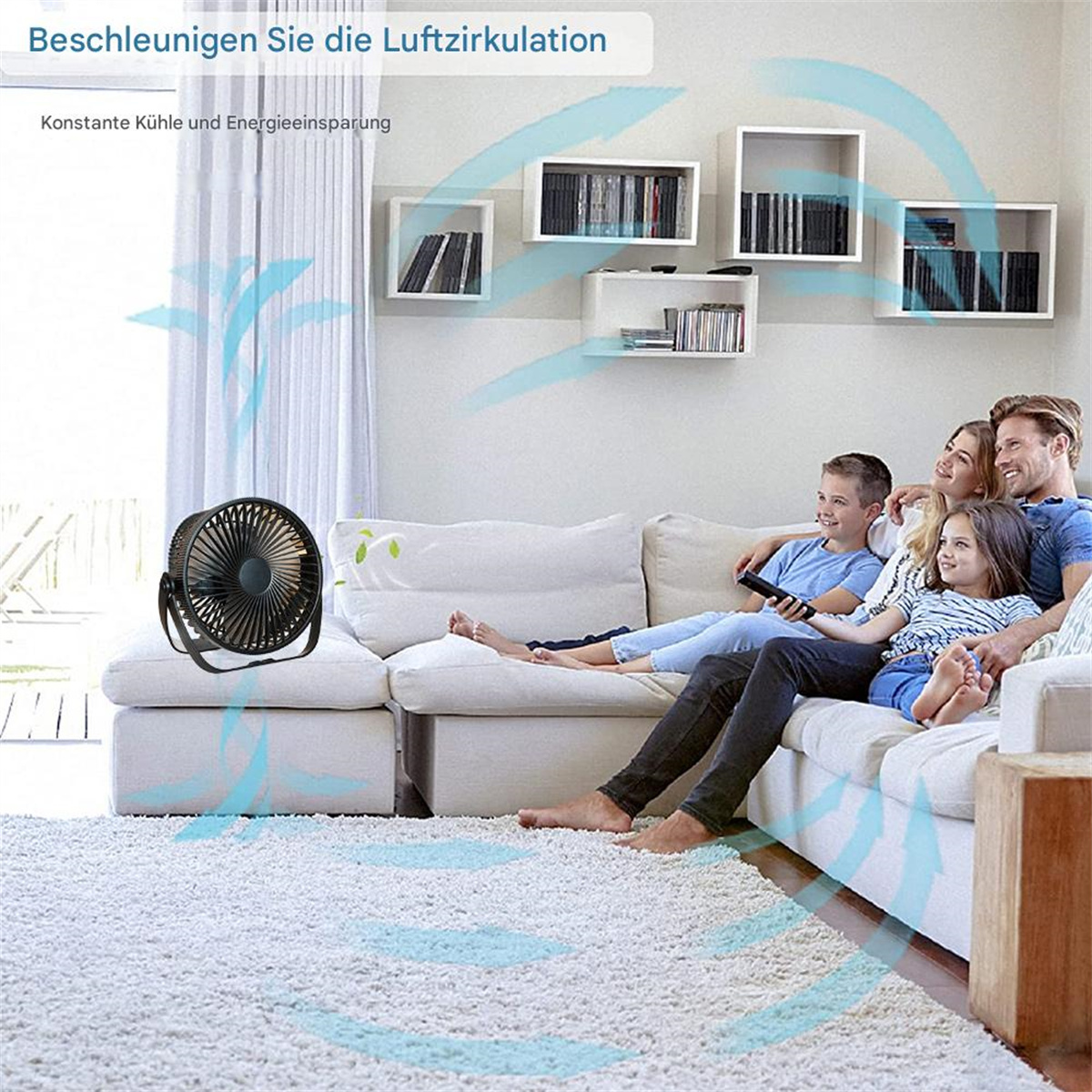 Eine Familie sitzt auf einem weißen Sofa und sieht fern. Ein schwarzer Ventilator steht davor, mit dargestellten Luftströmungen. Weiße Regale an der Wand.