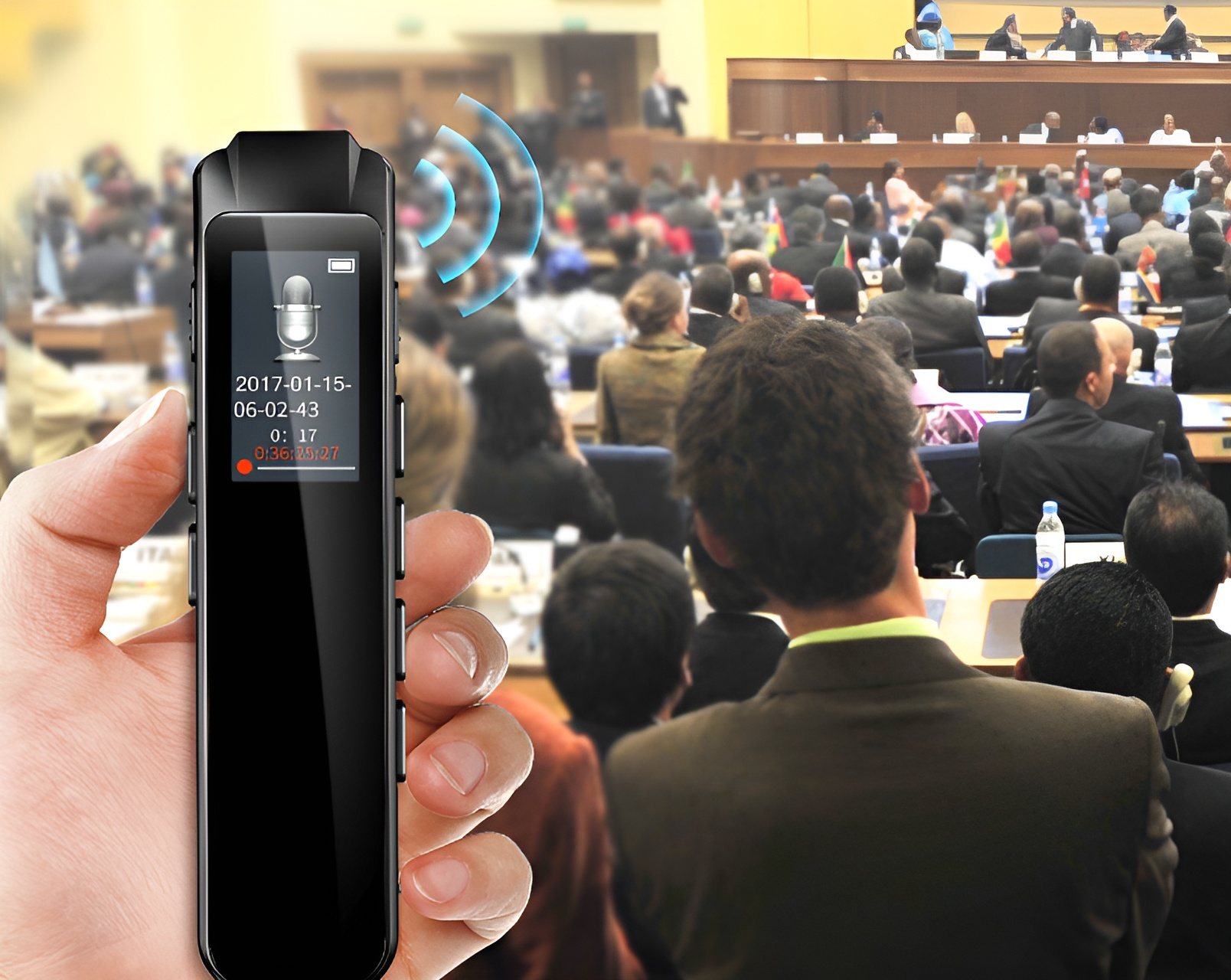 Hand hält ein Aufnahmegerät mit Mikrofon-Symbol, das eine Konferenz aufzeichnet. Menschen sitzen und hören zu. Blaue Signalwellen werden gezeigt.