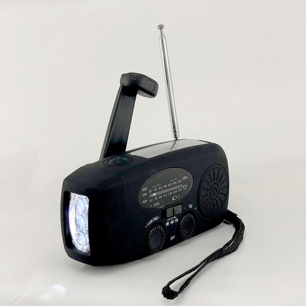 Ein schwarzes Kurbelradio mit Taschenlampe und Antenne. Es hat Knöpfe und einen Abstimmknopf. Auf der Seite hängt ein schwarzer Riemen.