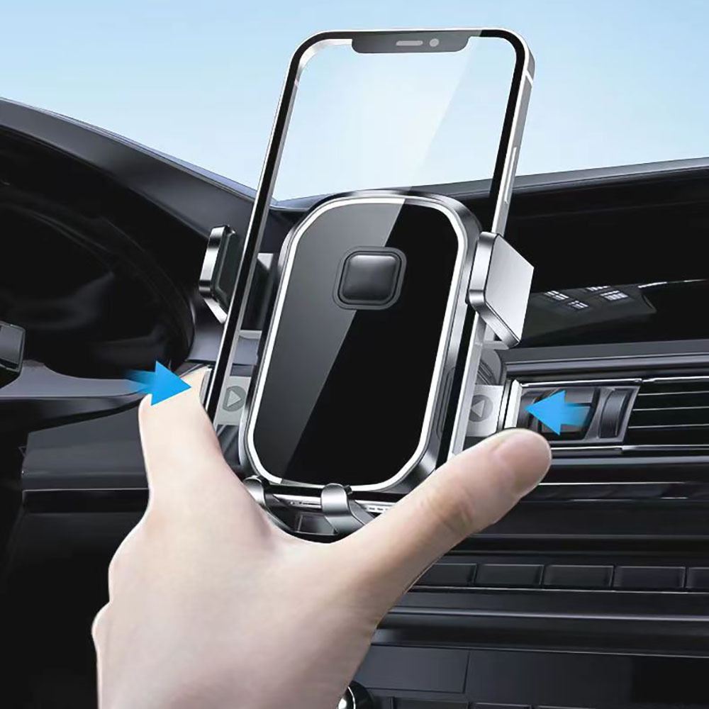 Eine Hand hält eine Autotelefonhalterung mit einem Telefon darin. Die Halterung ist silber und schwarz, im Armaturenbrett eines Autos.