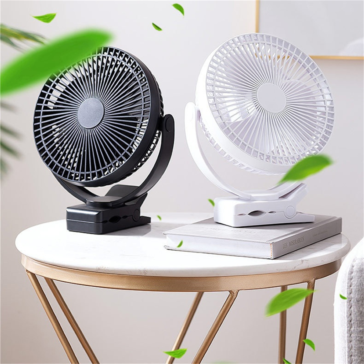 Zwei kleine Ventilatoren auf einem Tisch. Einer ist schwarz, der andere weiß. Grüne Blätter sind zu sehen.