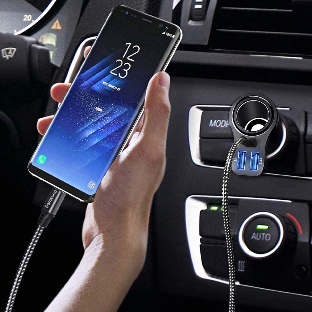 Eine Hand hält ein Samsung-Telefon, das an ein Autoladegerät angeschlossen ist. Das Telefon zeigt Uhrzeit und Datum an. Ladegerät hat USB-Anschlüsse.