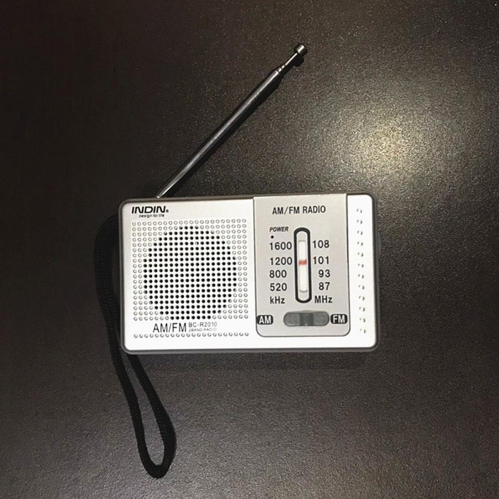 Ein kleines silbernes AM/FM-Radio mit schwarzer Antenne und Band auf dunkler Oberfläche. Das Radio zeigt Frequenzdetails.