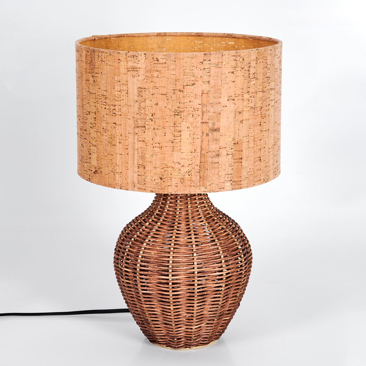 Eine Lampe mit einem gewebten braunen Sockel und einem zylindrischen Lampenschirm aus Kork. Der Hintergrund ist schlicht weiß.