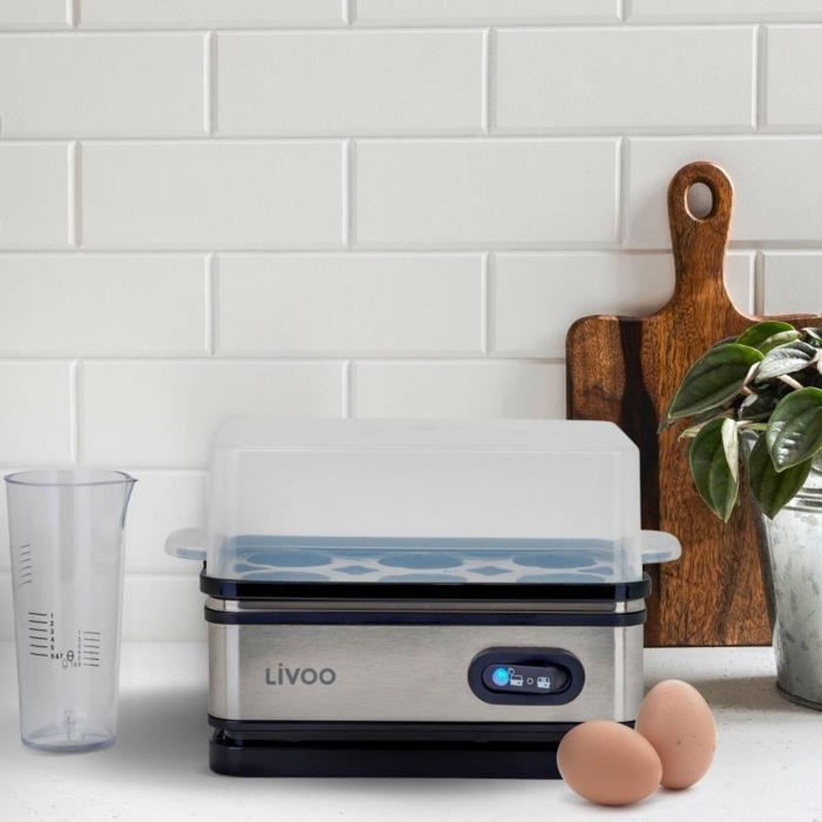 Urządzenie do gotowania jajek z jajkami na pierwszym planie. Miarka, deska do krojenia i roślina w tle.