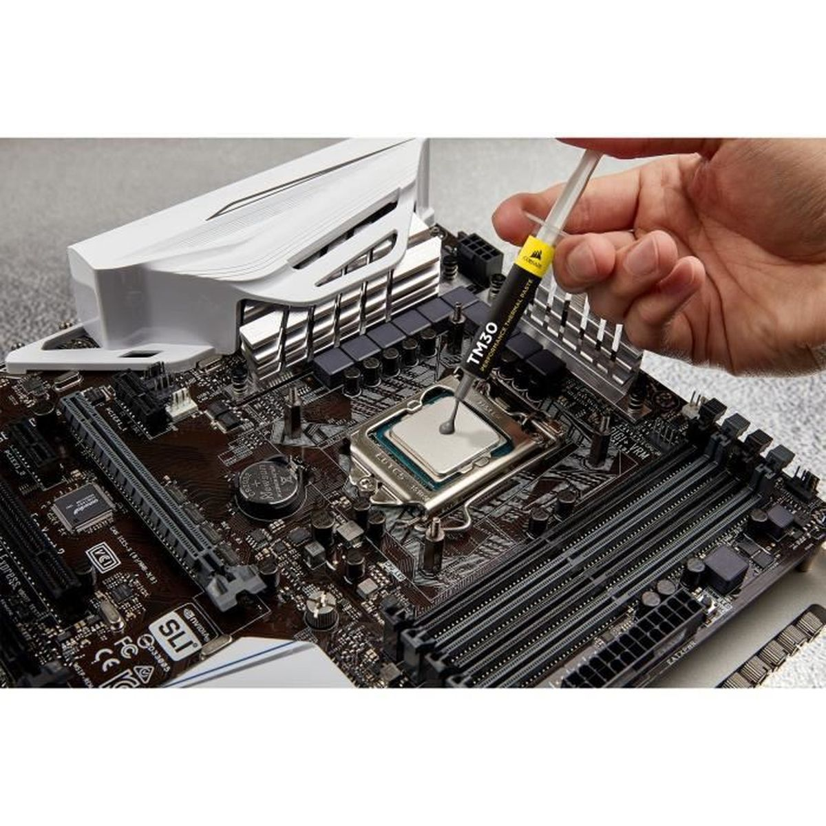 Eine Hand gibt Wärmeleitpaste auf eine CPU auf einem Motherboard. Die Szene umfasst einen weißen Kühlkörper und andere Computerkomponenten.