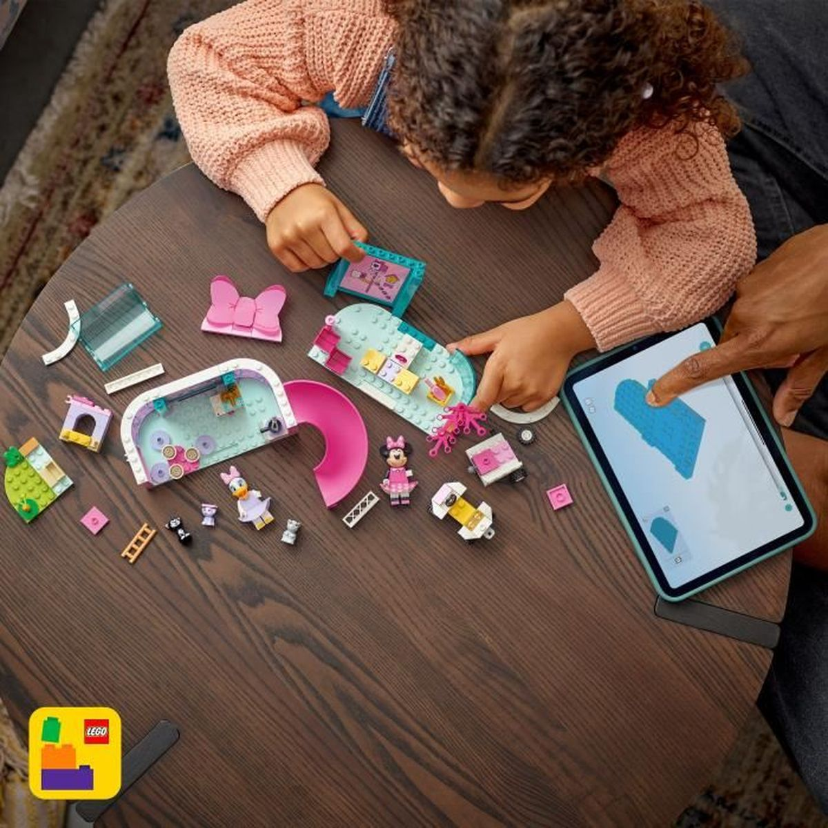 Dziecko i dorosły budują zestaw Lego na stole. Klocki Lego z Minnie Mouse, zjeżdżalnią i innymi kształtami są rozrzucone.