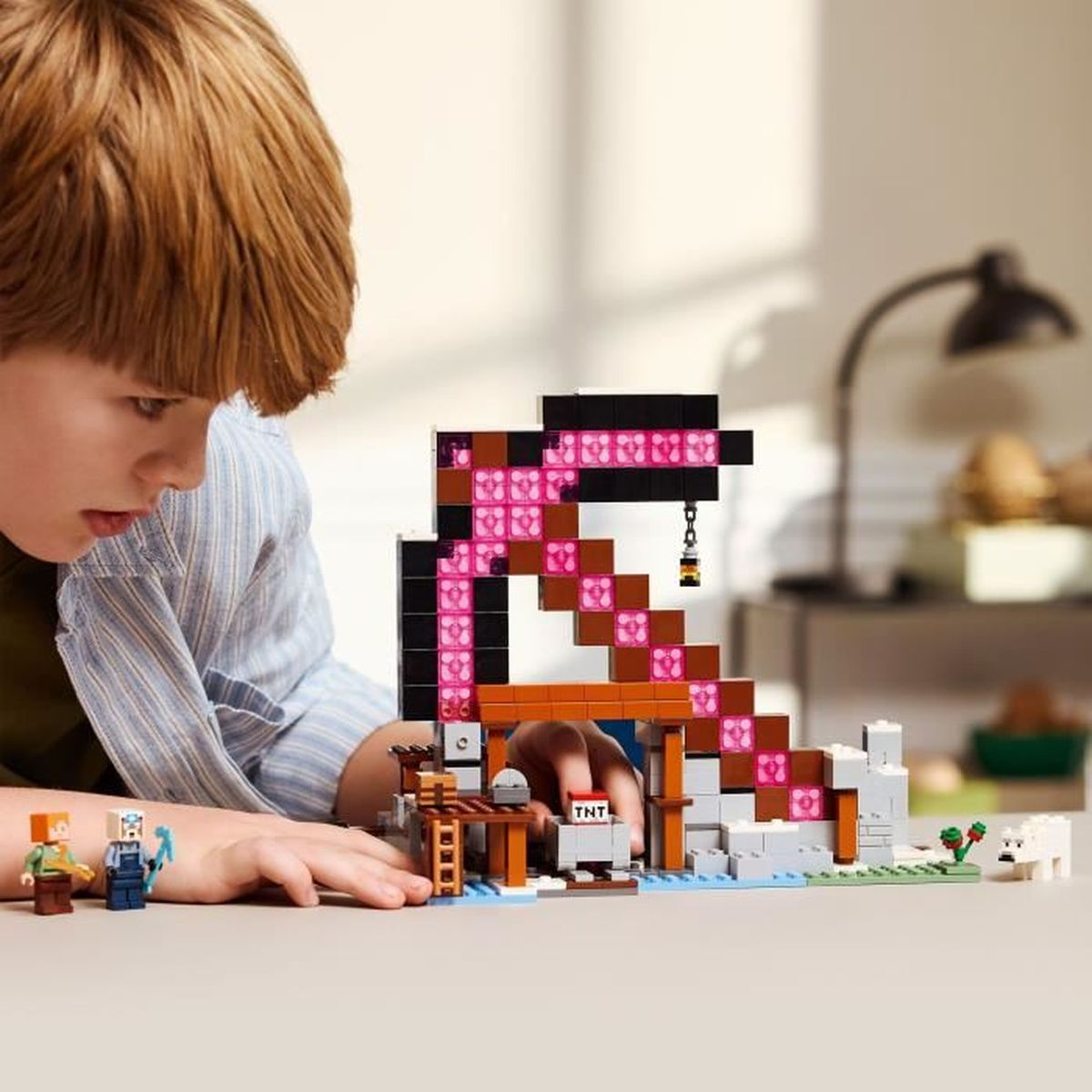 Dziecko patrzy na zestaw Lego Minecraft. Zestaw zawiera konstrukcję, minifigurki i blok TNT.