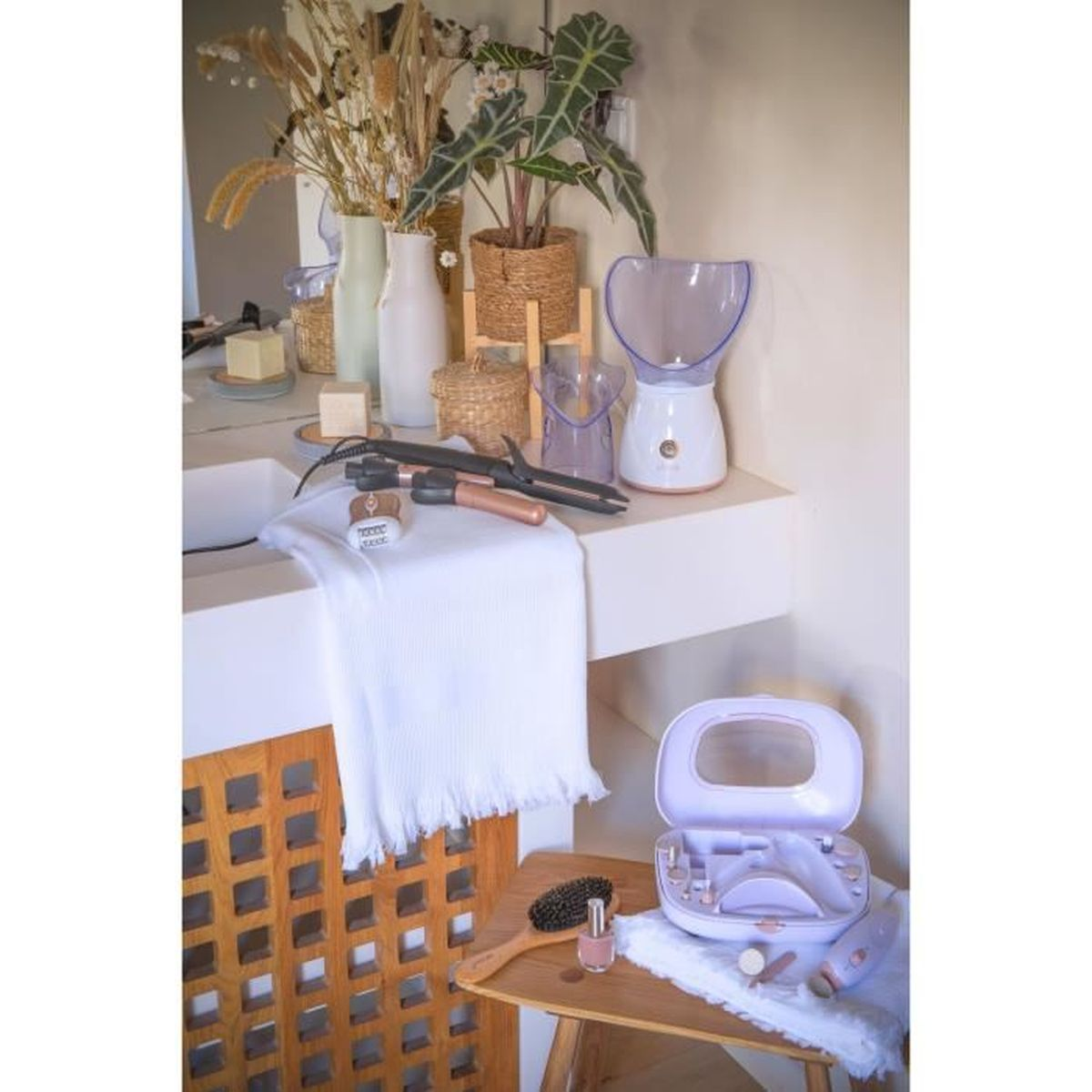 Scena bagno con prodotti di bellezza. Vaporizzatore, arricciacapelli, trousse trucco aperta, pennello, smalto per unghie, vasi e piante su un bancone bianco.
