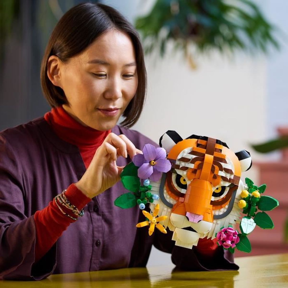 Kobieta z krótkimi włosami układa kwiaty na głowie tygrysa Lego. Tygrys jest pomarańczowy, biały i czarny, z dekoracjami kwiatowymi.