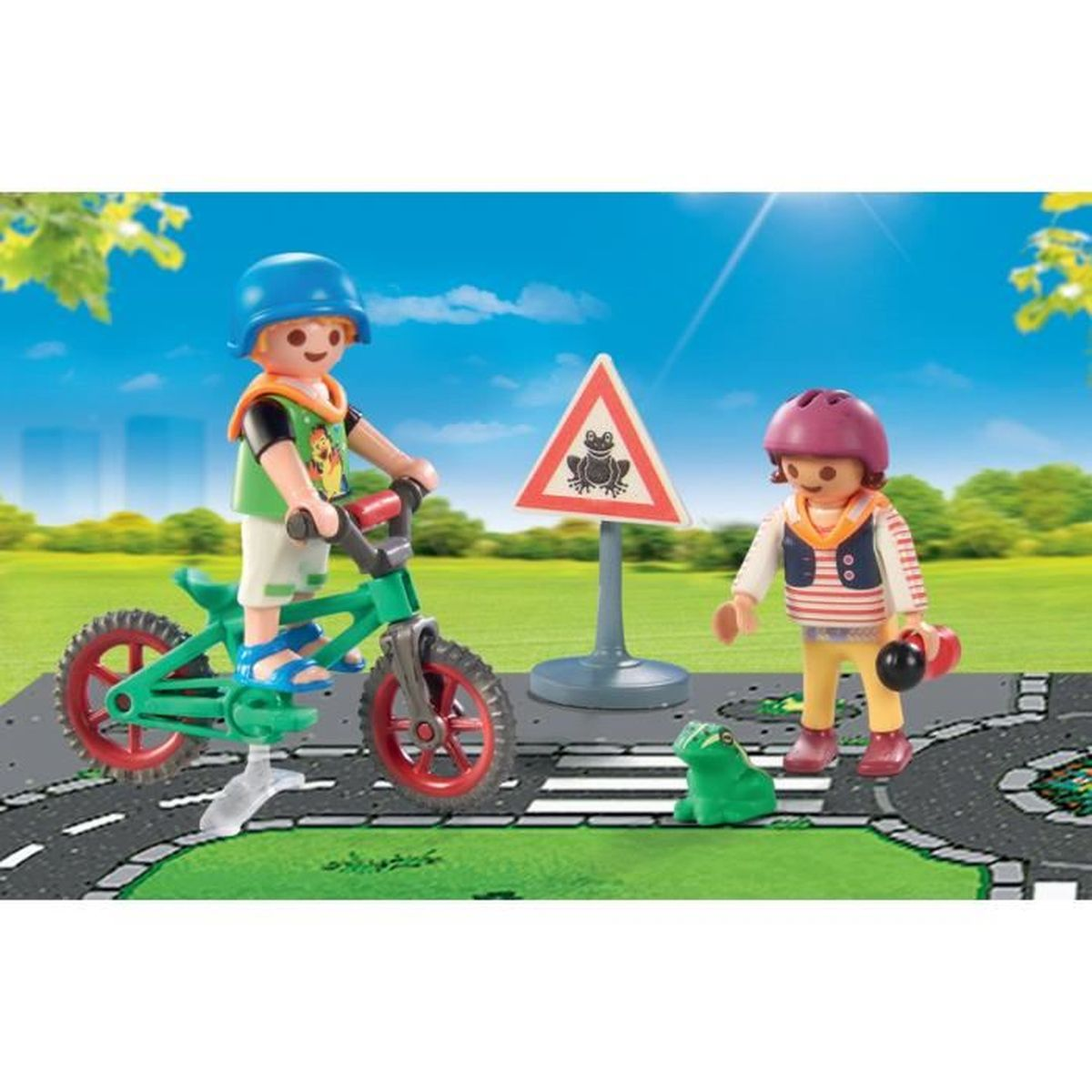 Ein Kind fährt Fahrrad. Ein anderes Kind steht in der Nähe eines Frosch-Verkehrszeichens und eines Spielzeugfroschs. Im Hintergrund sind Straße und blauer Himmel zu sehen.