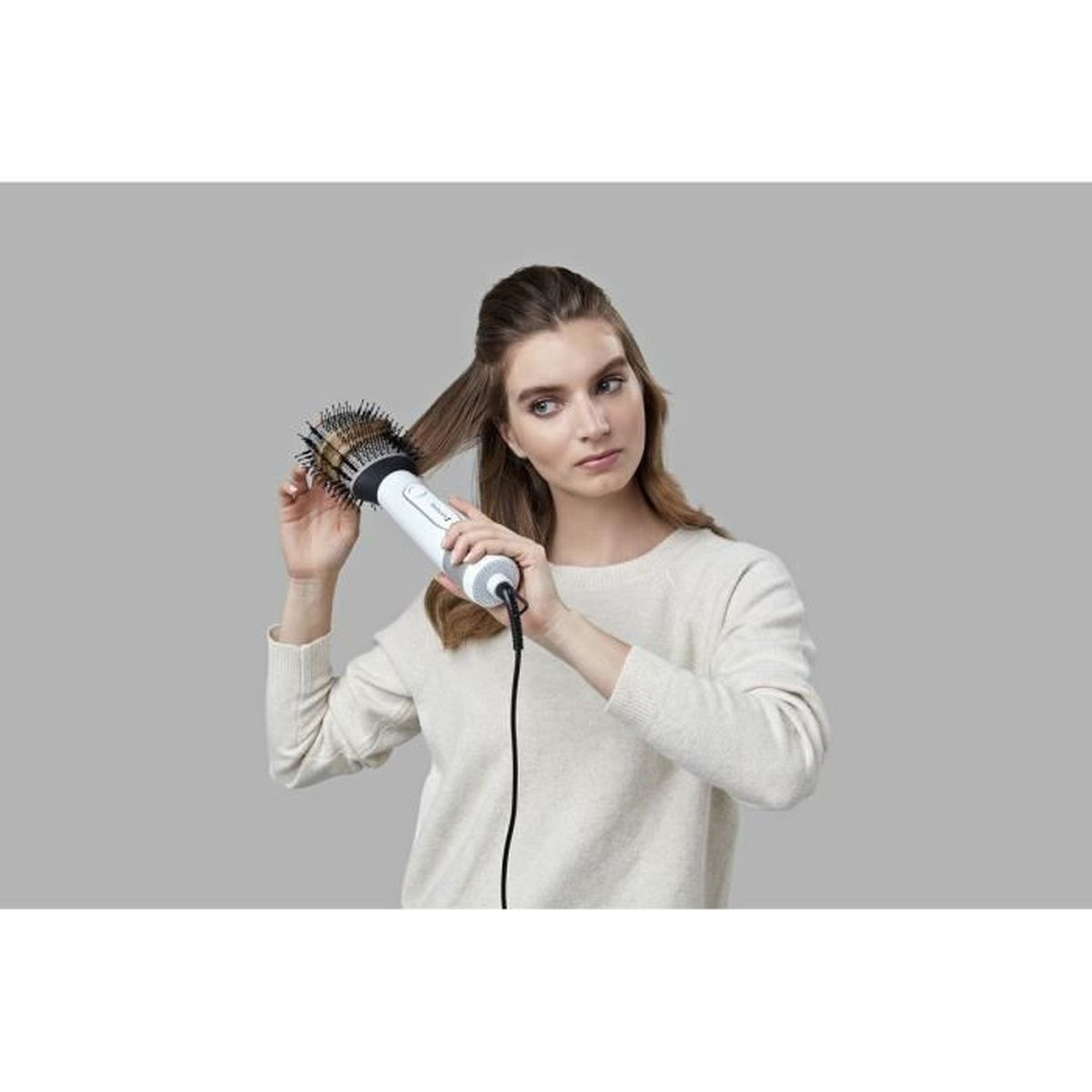 Kobieta stylizuje włosy biało-czarną szczotką. Ma na sobie kremowy sweter.