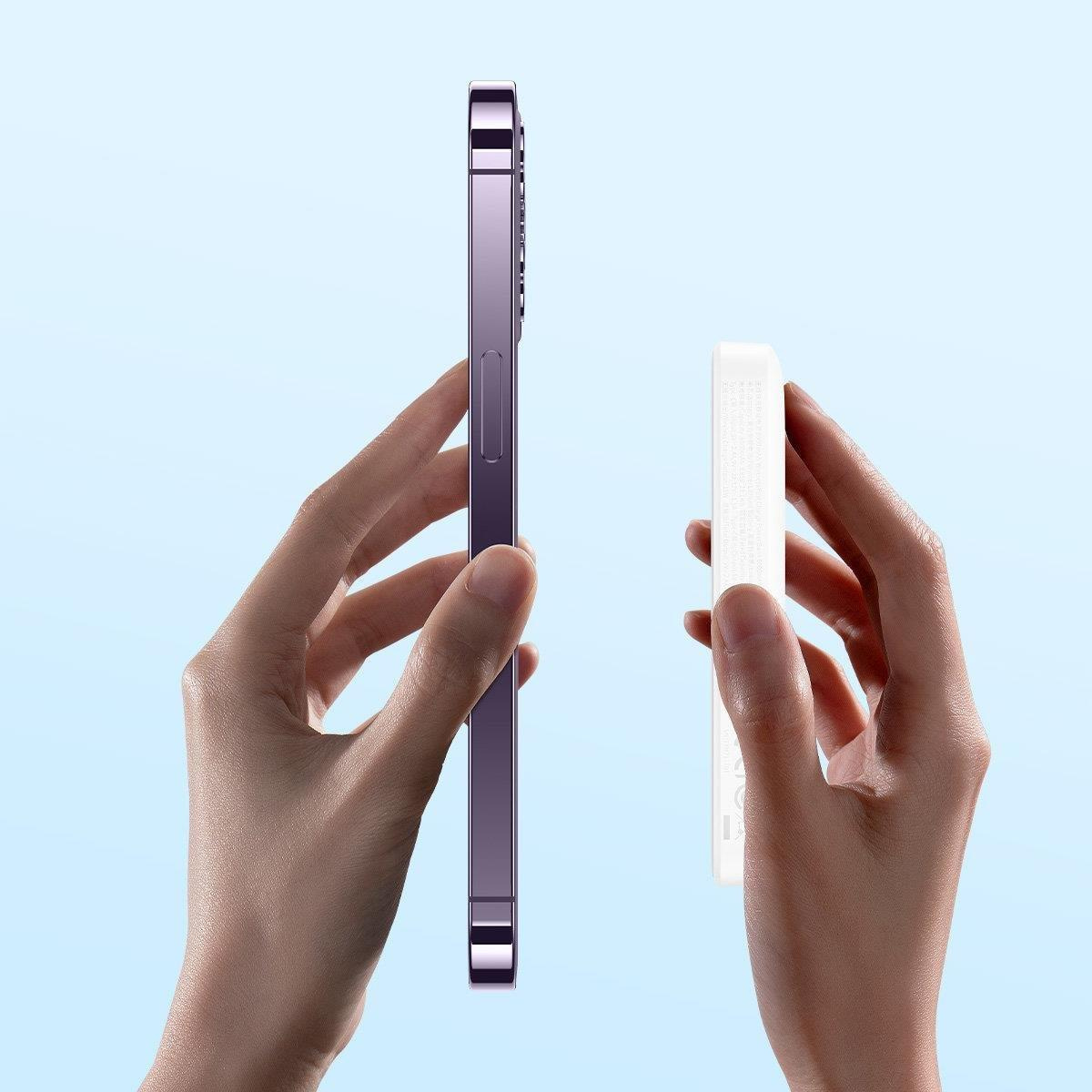 Ręce trzymają fioletowy telefon i biały power bank na jasnoniebieskim tle.