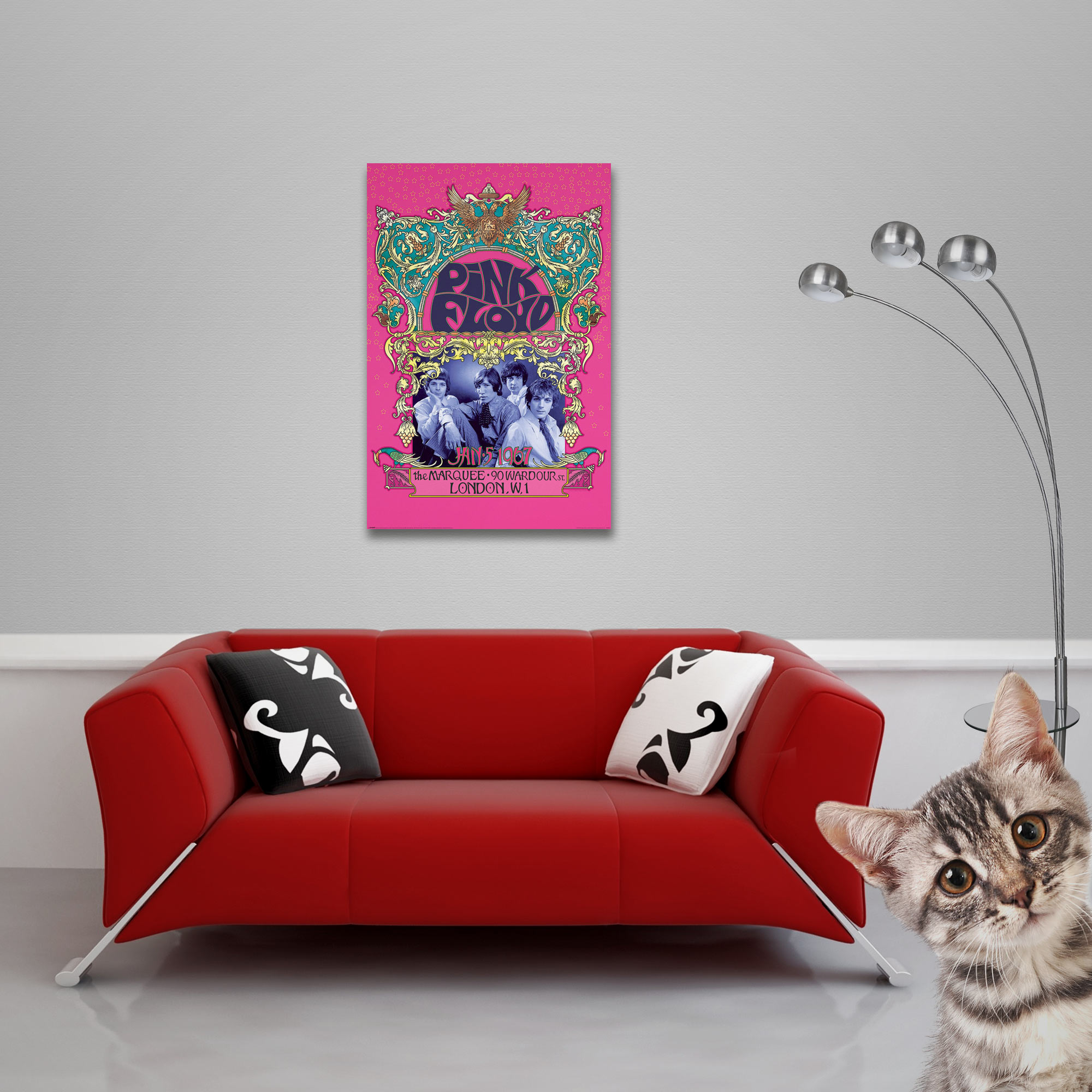 Ein Pink-Floyd-Poster hängt über einem roten Sofa mit Kissen. Eine Katze lugt von rechts hervor.