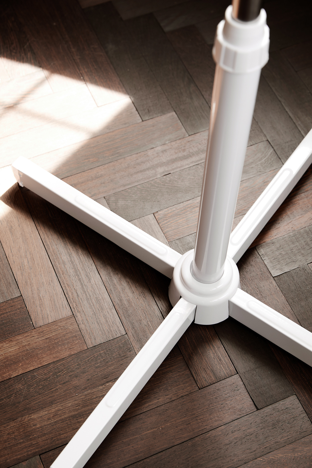 White metal stand base on a wooden floor. Sunlight illuminates the scene. The base has four legs and a central pole.