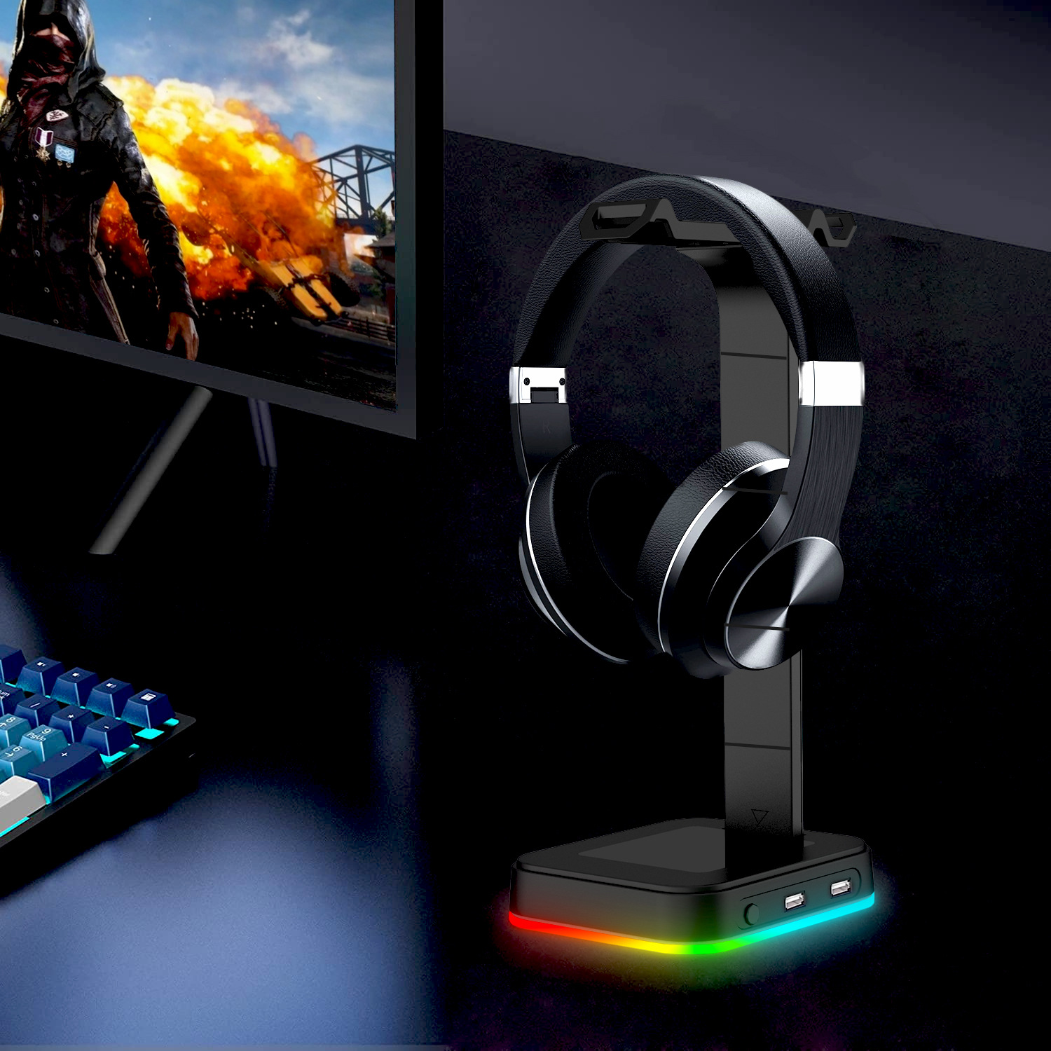 Schwarze Kopfhörer auf einem Ständer mit farbenfroher Basis. Monitor zeigt eine Spielszene. Tastatur links.