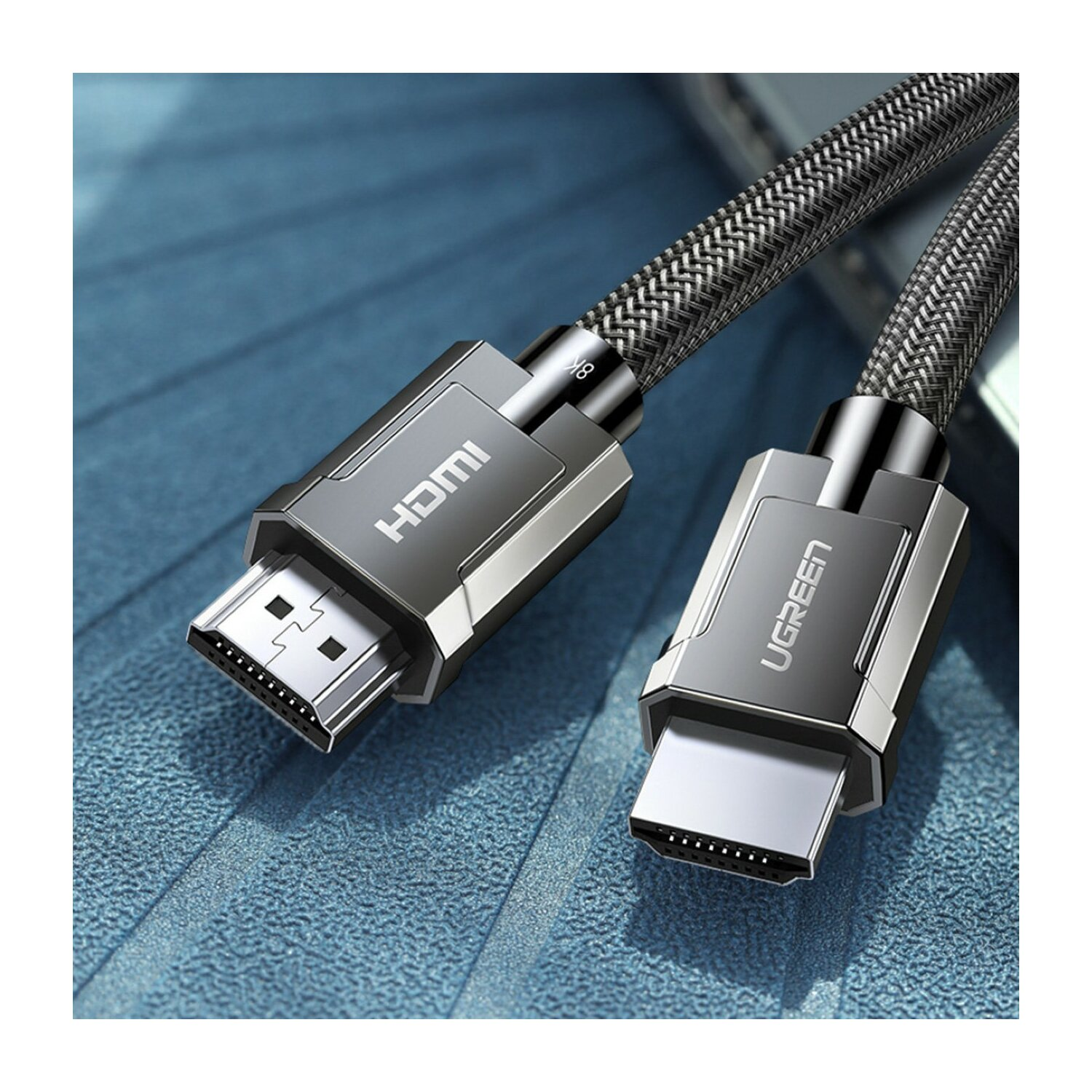 Dwa kable HDMI z metalowymi złączami i plecionymi szarymi kablami leżą na niebieskiej, teksturowanej powierzchni. Jedno złącze ma etykietę HDMI.