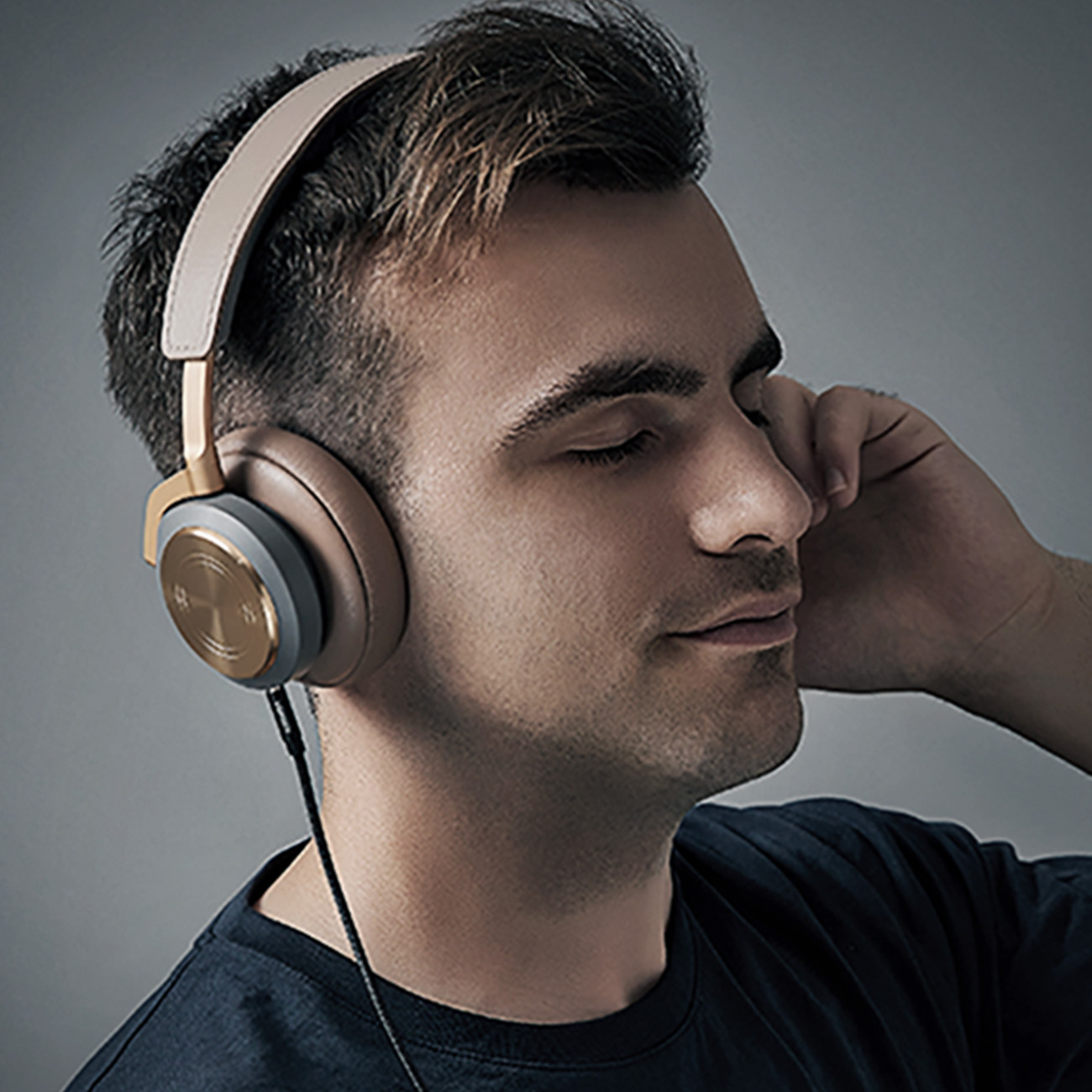 Mężczyzna ze słuchawkami słucha muzyki. Ma brązowe włosy i zamknięte oczy. Słuchawki są złote i brązowe.