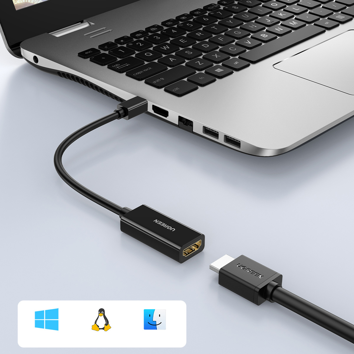 Laptop podłączony do czarnego adaptera HDMI za pomocą czarnego kabla. Adapter jest podłączony do kabla USB-C. Ikony Windows, Linux i Mac poniżej.