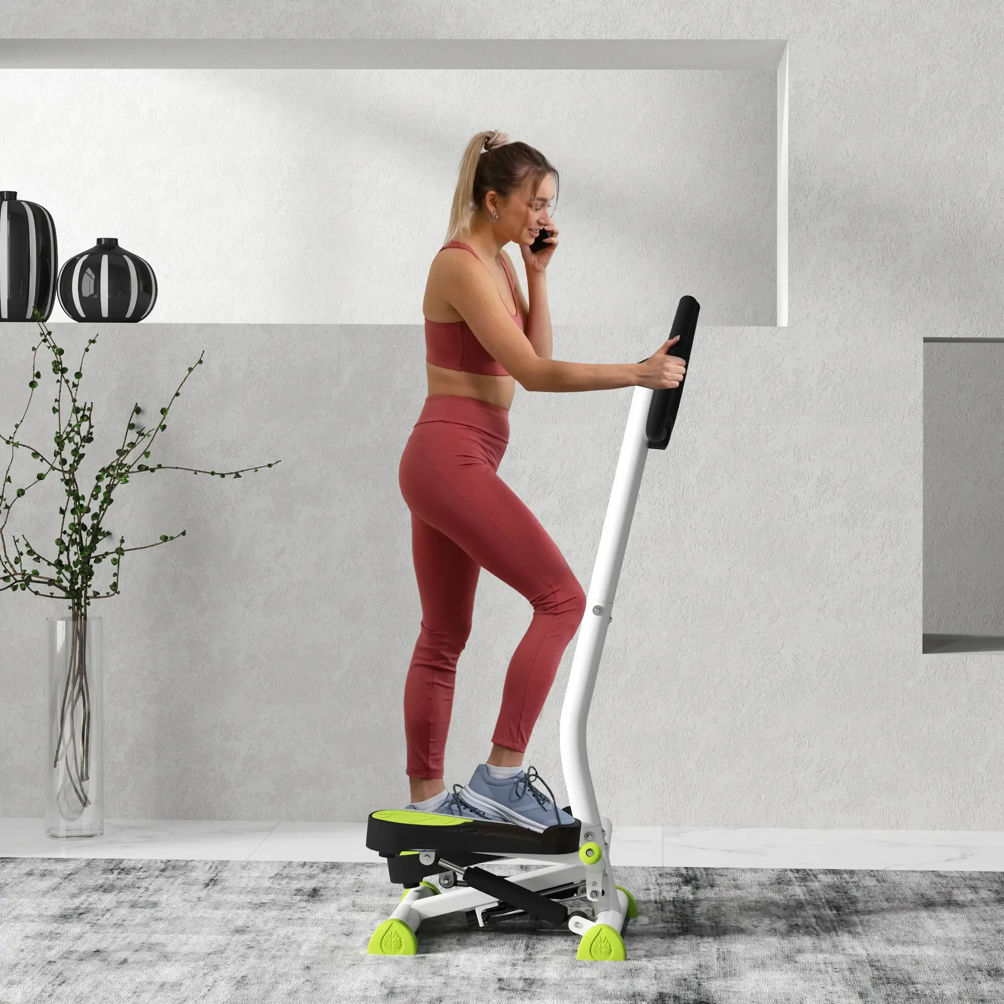 Frau in roter Trainingskleidung telefoniert, während sie einen Stepper in einem modernen weißen Raum benutzt.