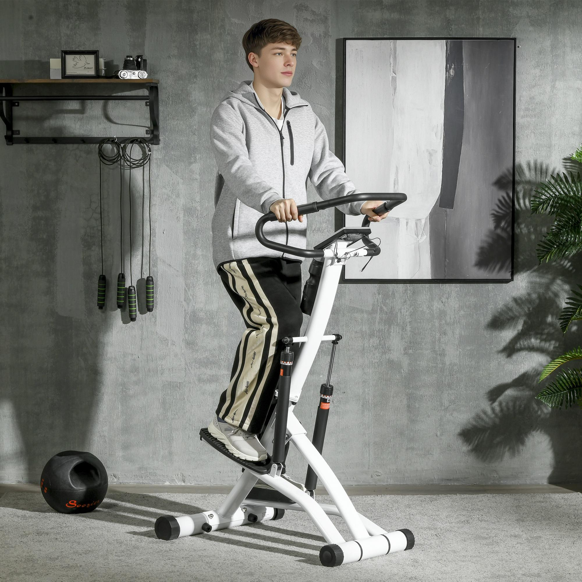 Ein Mann trainiert auf einer weißen Stepper-Maschine. Er trägt einen grauen Kapuzenpullover und schwarze Hosen. Ein Gemälde und Springseile sind sichtbar.