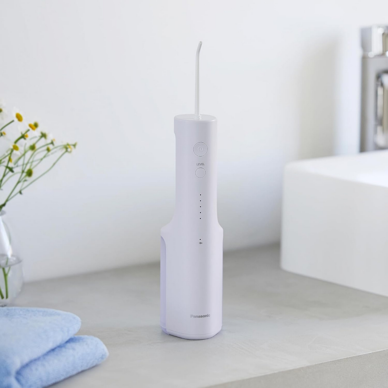 Ein weißer Panasonic-Wasserflosser steht auf einer Arbeitsplatte. Auf der linken Seite eine Blumenvase und blaue Handtücher. Rechts ein Waschbecken.
