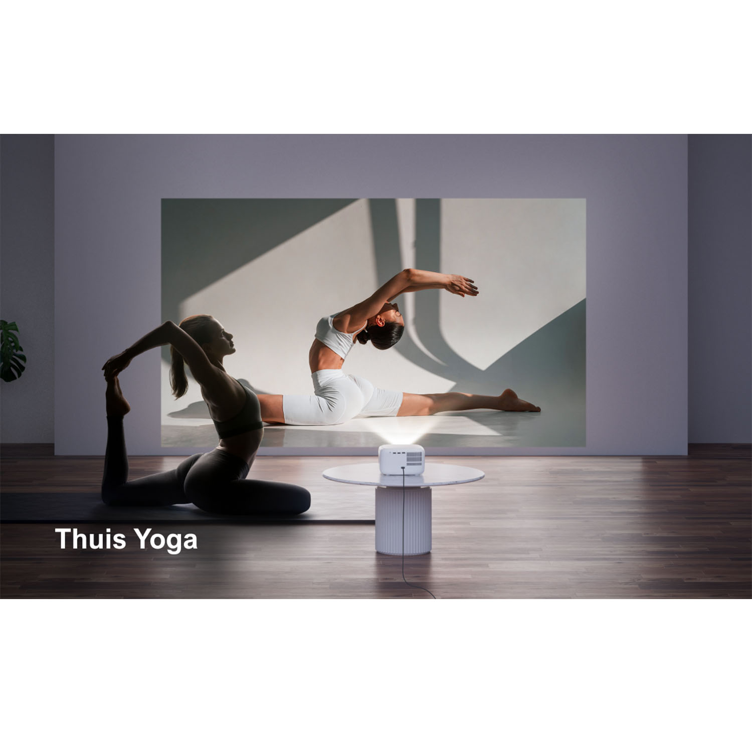 Deux femmes font du yoga. L'une porte une tenue blanche sur un écran. L'autre porte une tenue sombre sur un tapis. Un projecteur au premier plan.
