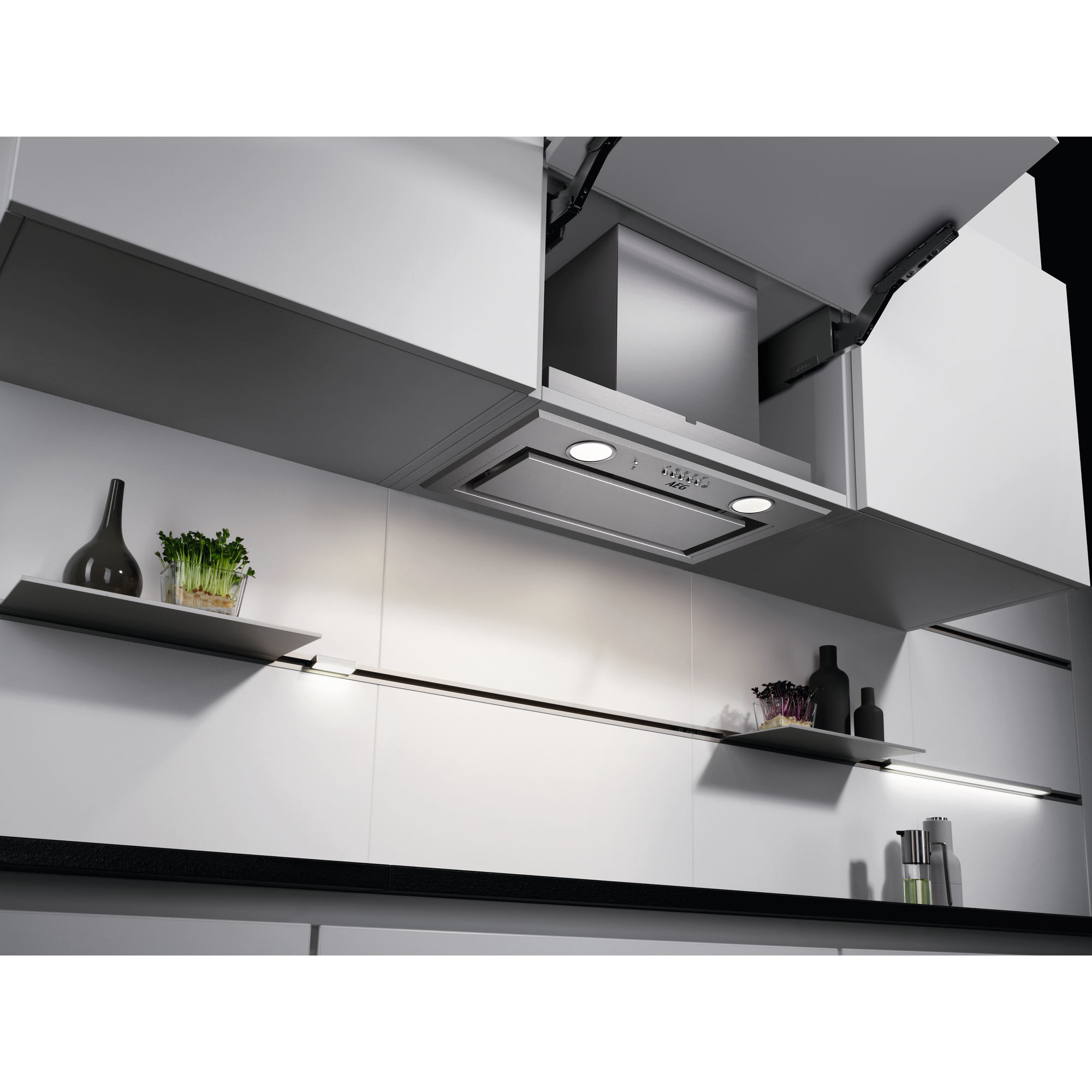 Cucina con mobili bianchi, cappa in acciaio inox, mensole con decorazioni. Piano di lavoro e sfondo neri, luci brillanti.