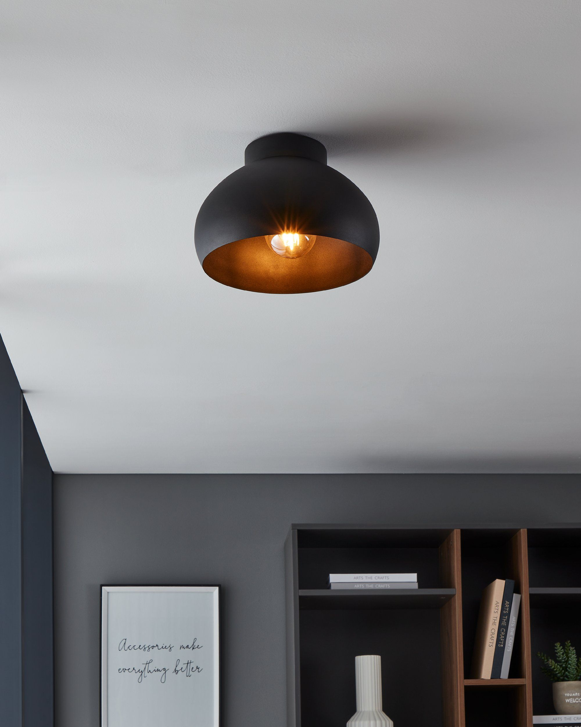 Una lampada da soffitto nera con interno dorato è accesa. C'è un poster con scritto 'Gli accessori rendono tutto migliore' sul muro.